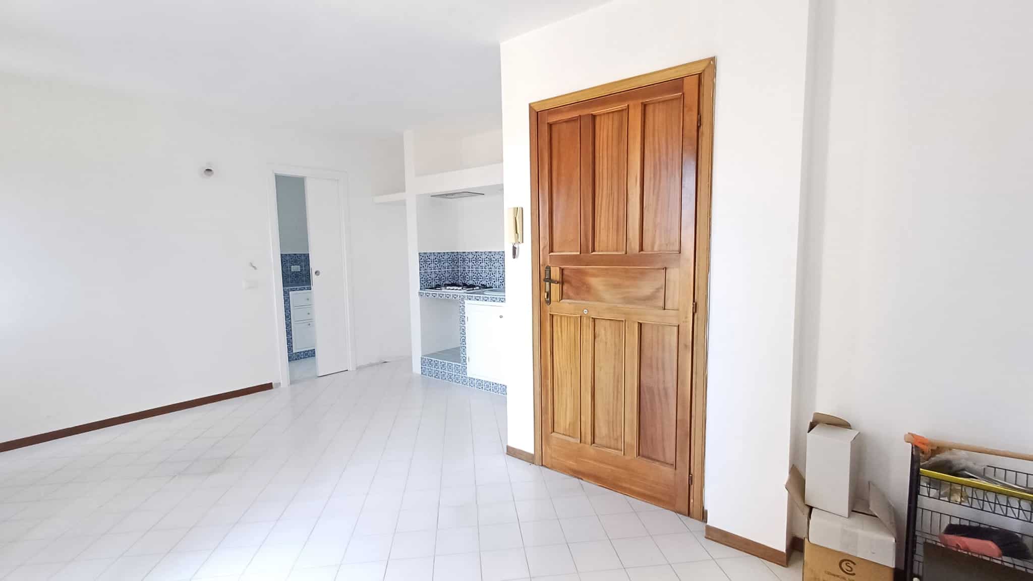Ampio soggiorno luminoso con pareti bianche, pavimento in piastrelle bianche e porta in legno massiccio, ambiente moderno e accogliente.