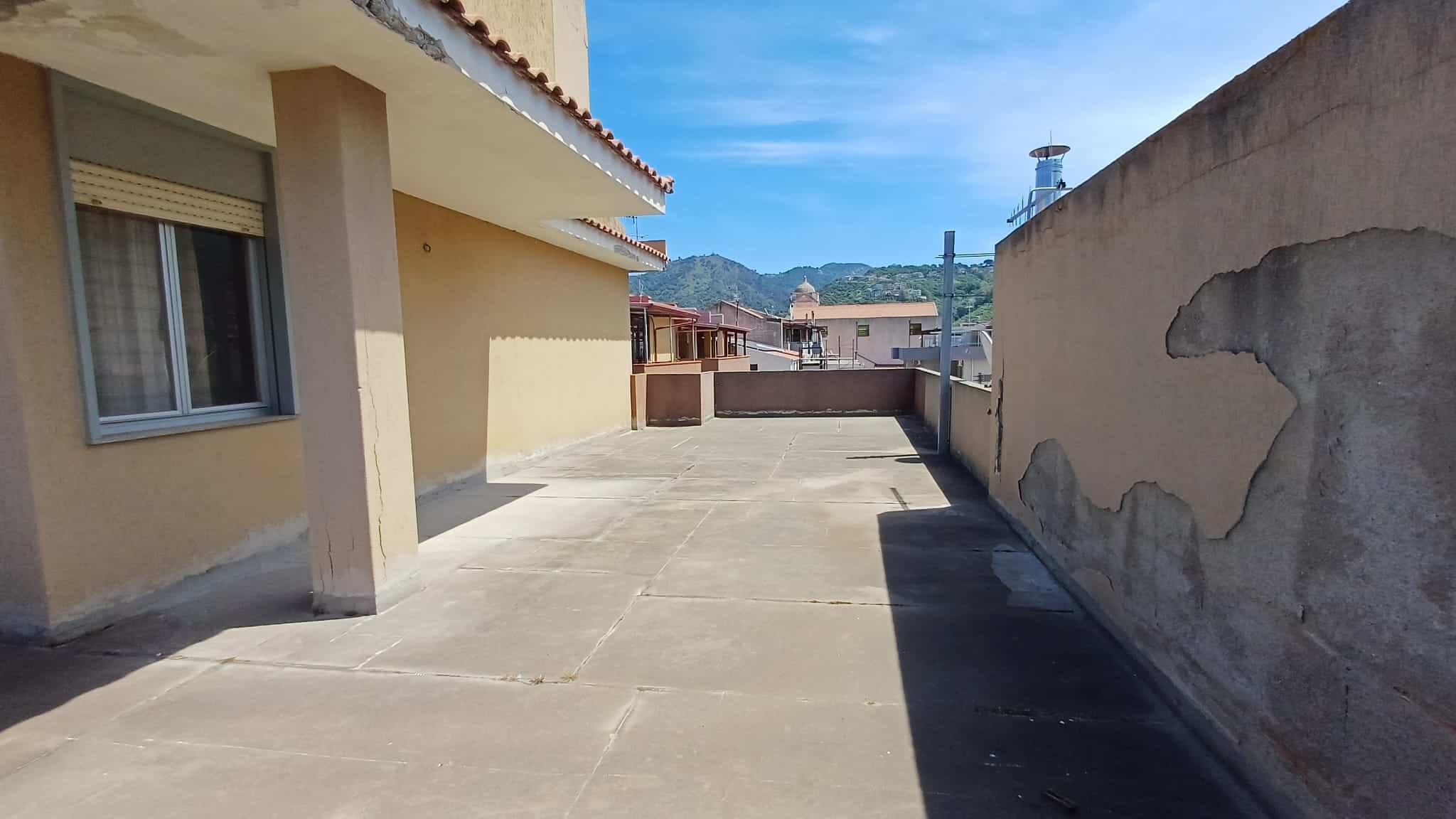 Ampio terrazzo esterno con vista sulle montagne, ideale per relax e attività all'aperto, situato in un complesso residenziale a NextCasa, con pavimentazione in cemento e pareti di privacy.