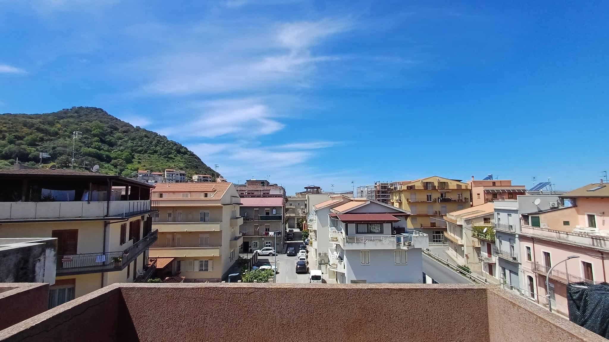 Balcone con vista sulla città e sulle colline, case residenziali e strade trafficate sotto un cielo azzurro con nuvole leggere, in un quartiere urbano di un'area residenziale italiana.
