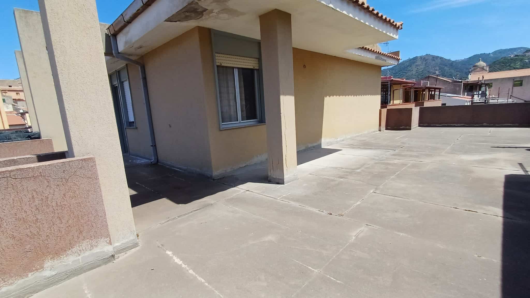 Ampio terrazzo esterno di una casa moderna con vista sulle montagne, pavimentato in cemento e spazio ideale per relax e attività all'aperto.