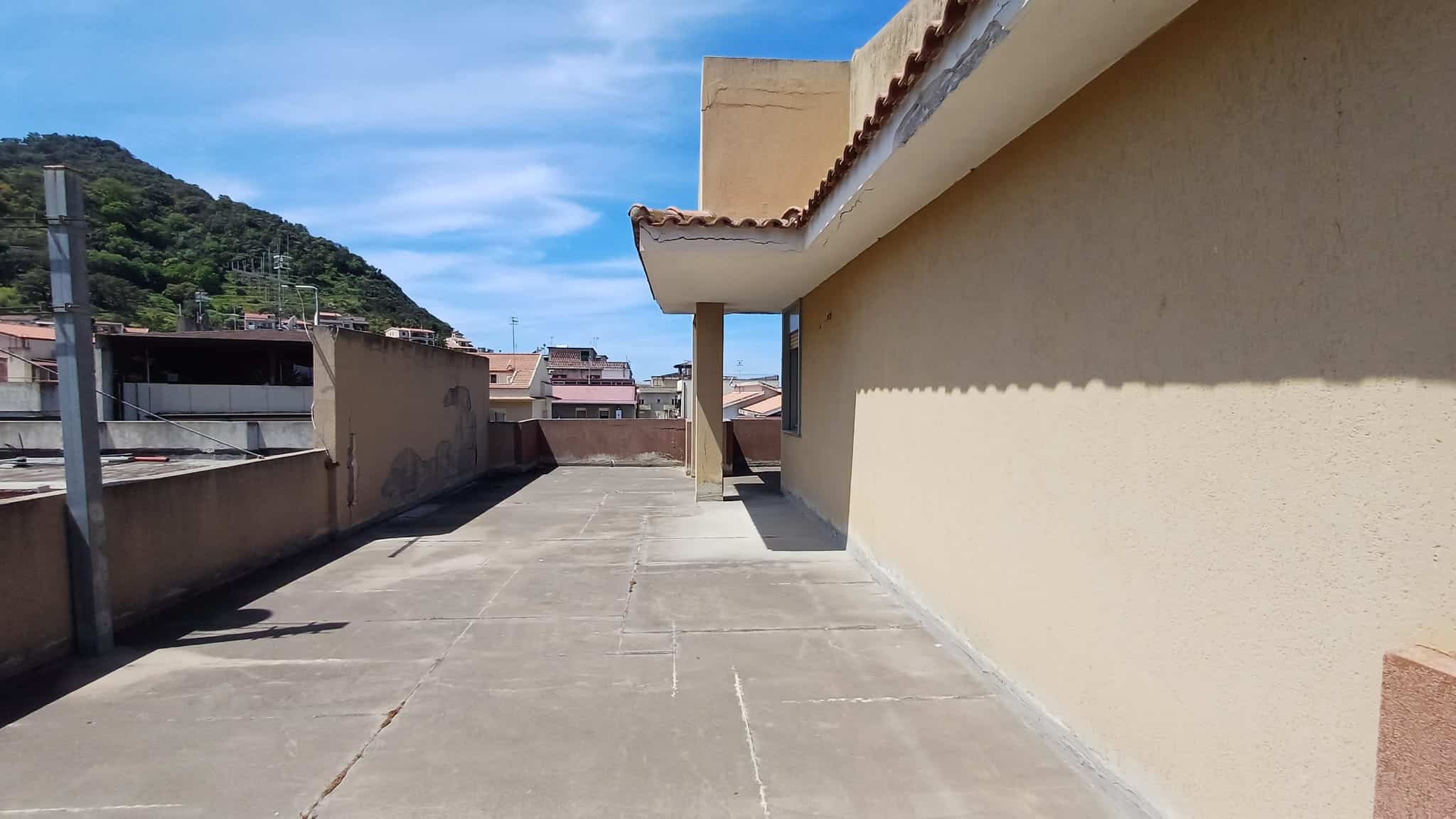 Ampio terrazzo all'aperto con vista sul paesaggio urbano e sulla collina, ideale per relax e attività all'aperto, con superficie pavimentata e protezione solare parziale.