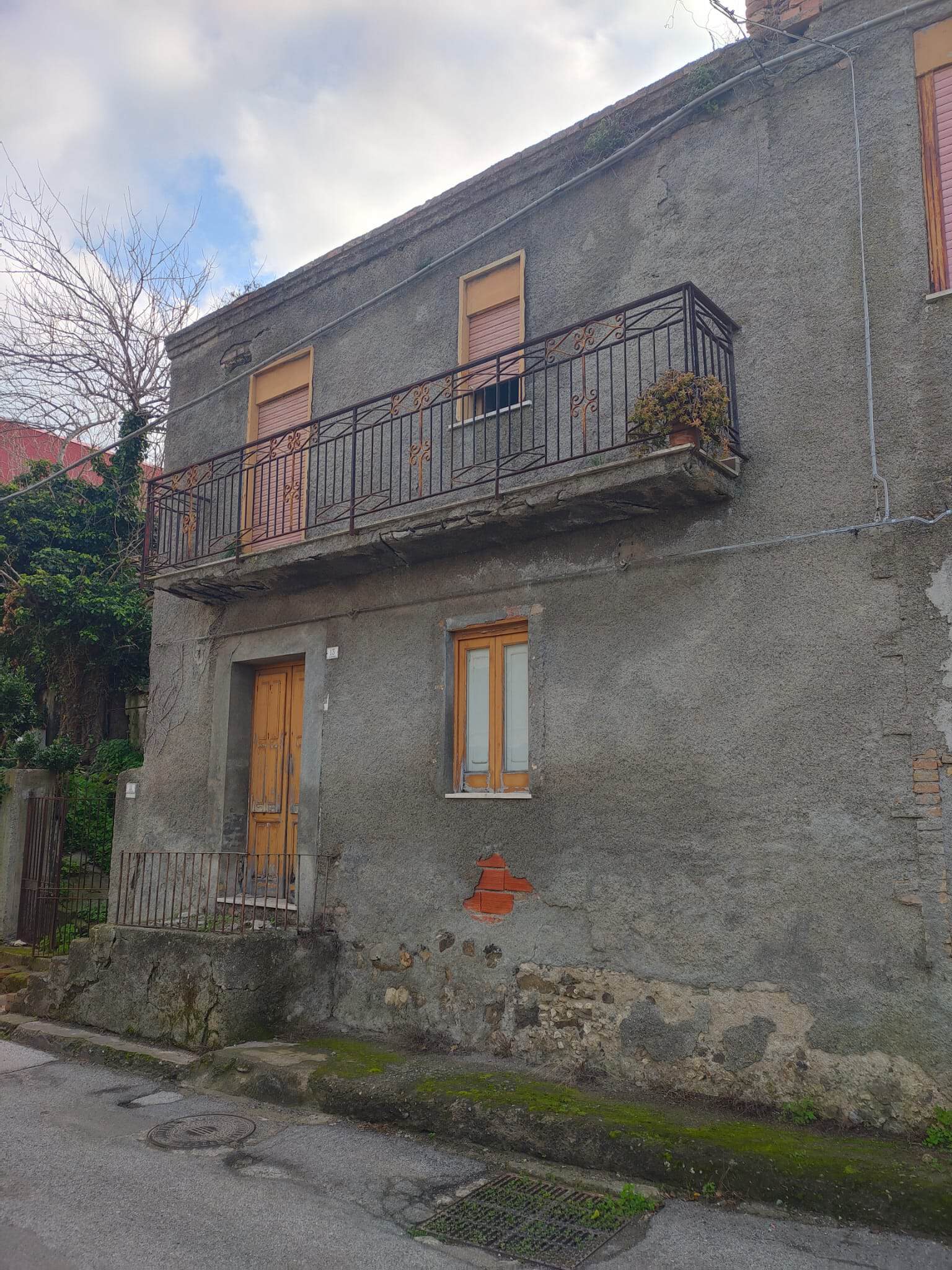 Balcone in ferro battuto su edificio residenziale in stile rustico, con pareti in pietra e finestre con infissi in legno, situato in zona urbana.