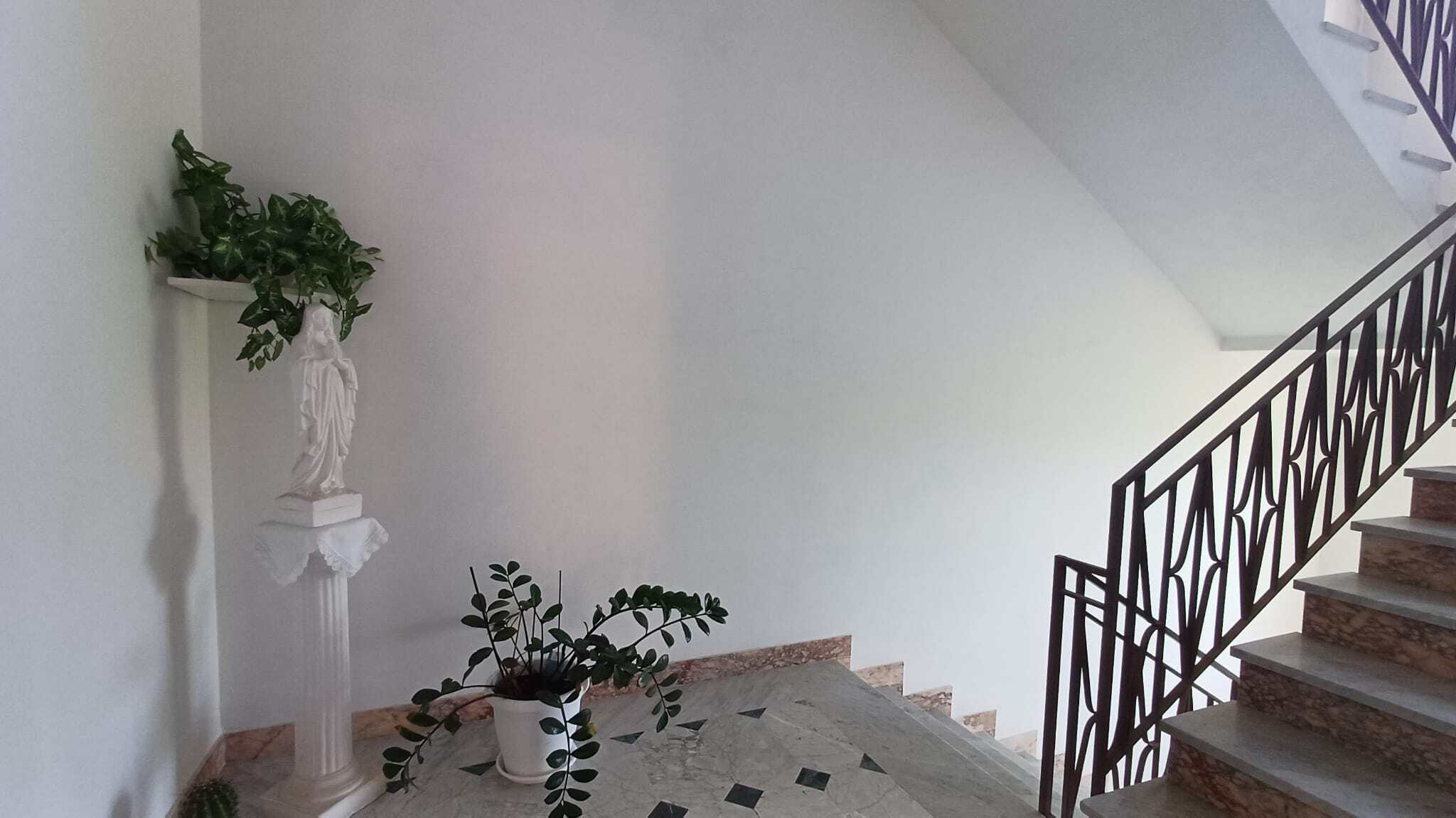 Elegante ingresso con scale in marmo e ringhiera in ferro battuto, decorato con piante verdi e statua classica, ideale per immobili di lusso e residenze di prestigio.