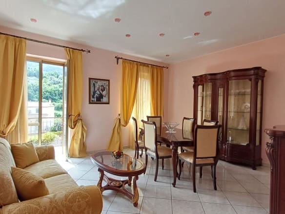 Elegante soggiorno con grandi finestre, tende gialle e arredi classici in legno, ideale per vivere momenti di relax e convivialità in un ambiente luminoso e accogliente.