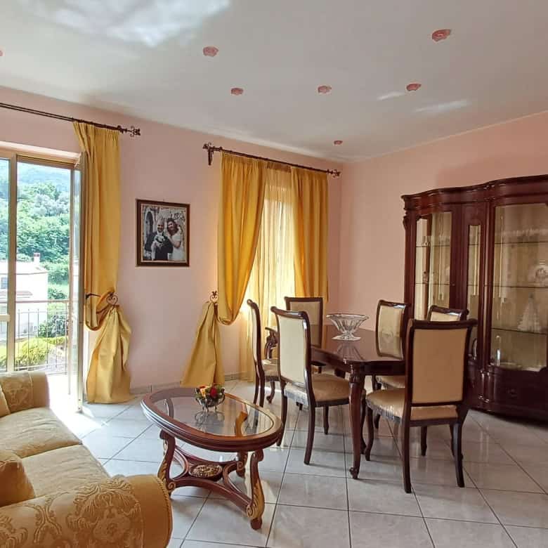 Elegante soggiorno con grandi finestre, tende gialle e arredi classici in legno, ideale per vivere momenti di relax e convivialità in un ambiente luminoso e accogliente.
