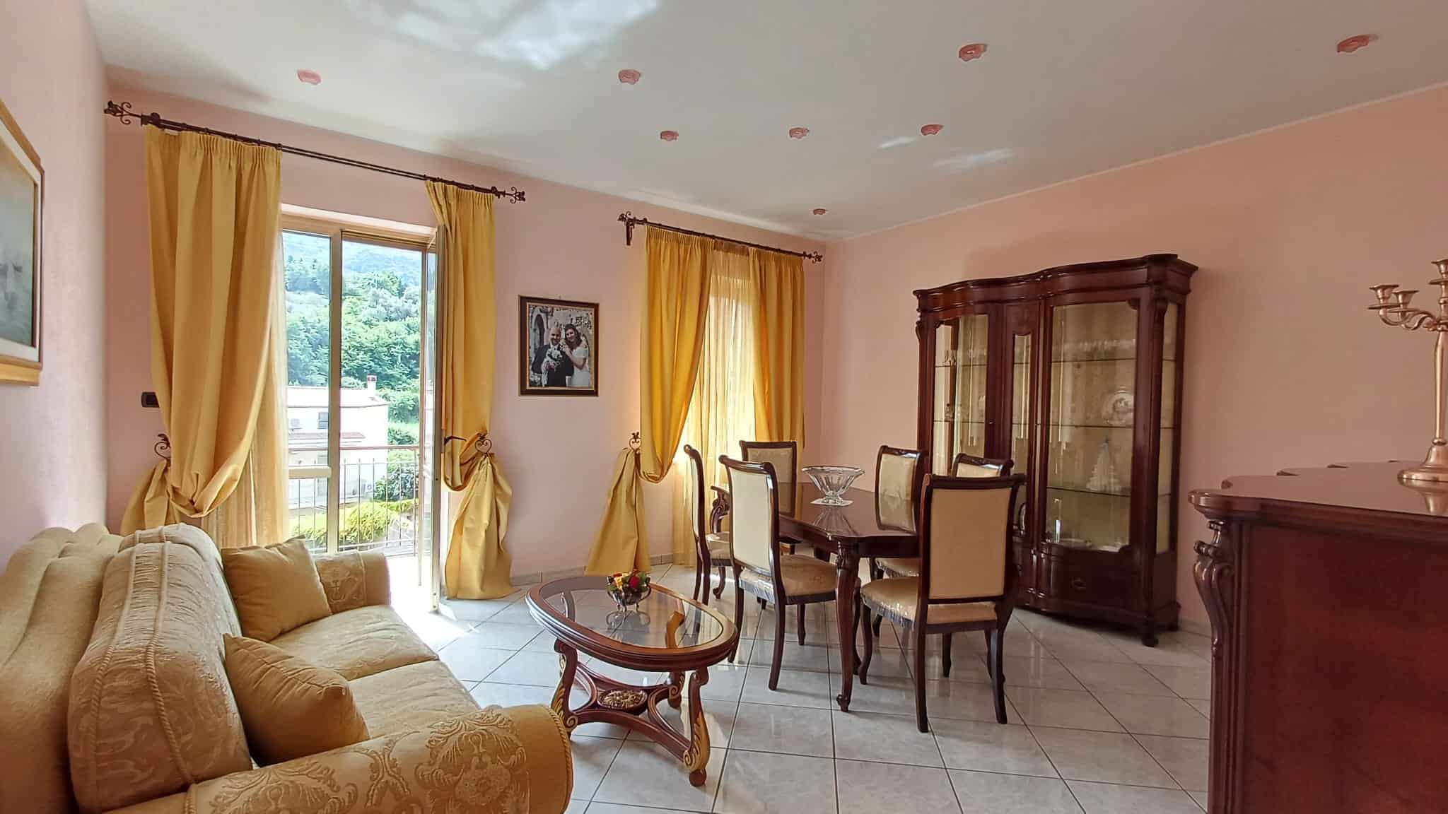 Elegante soggiorno con grandi finestre, tende gialle e arredi classici in legno, ideale per vivere momenti di relax e convivialità in un ambiente luminoso e accogliente.