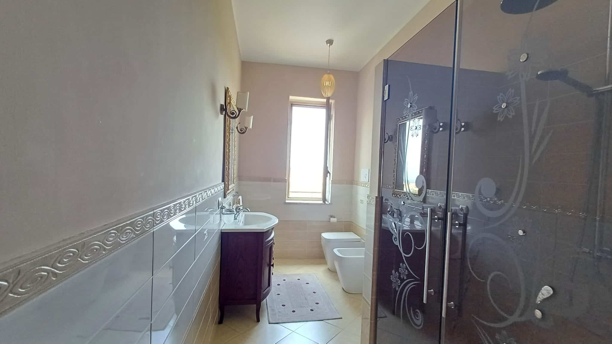 Ampia stanza da bagno moderna con doccia in vetro, lavabo elegante e finestra luminosa, ideale per case di alta qualità e comfort abitativo.