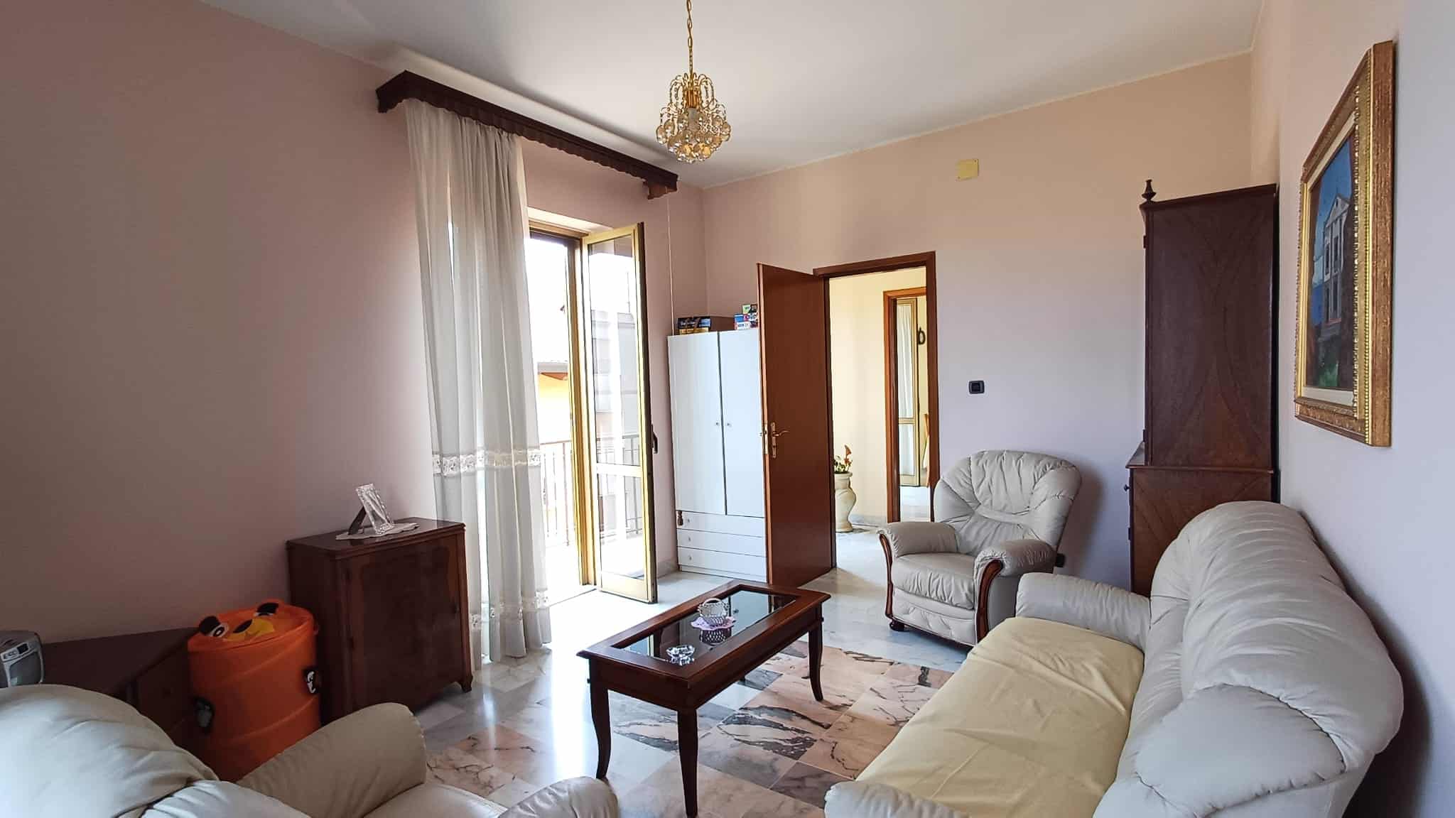 Ampia zona living con divani e poltrona, illuminata da luce naturale, in un appartamento in affitto o vendita a NextCasa, con accesso a balcone e arredamento classico.