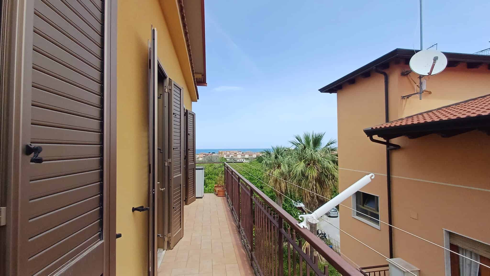 Balcone con vista mare e palme, case residenziali in stile mediterraneo, ambiente esterno soleggiato e tranquillo, ideale per relax e vita all'aperto.