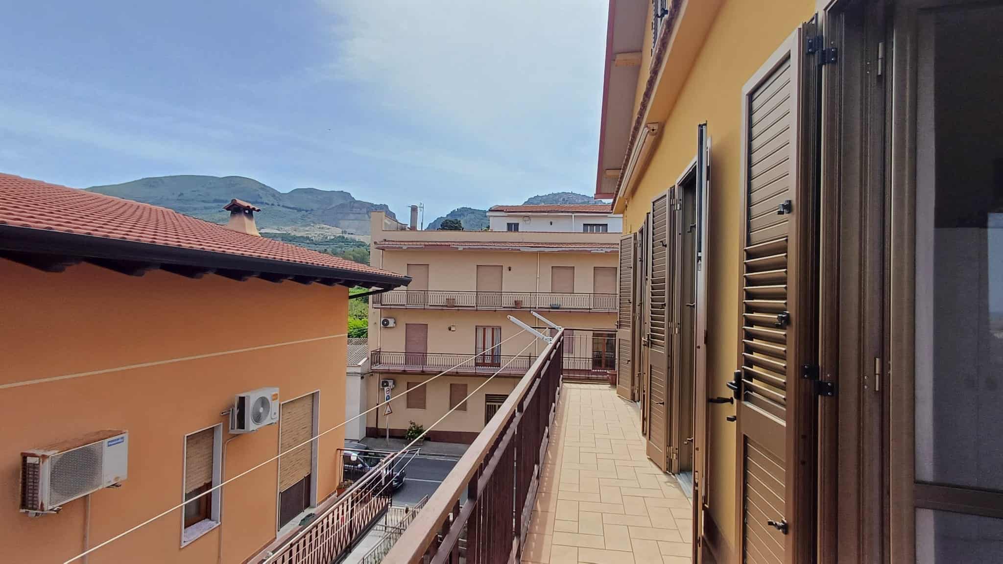 Balcone di un appartamento con vista sulle case e le montagne, con persiane in legno e aria condizionata, in un quartiere residenziale tranquillo.