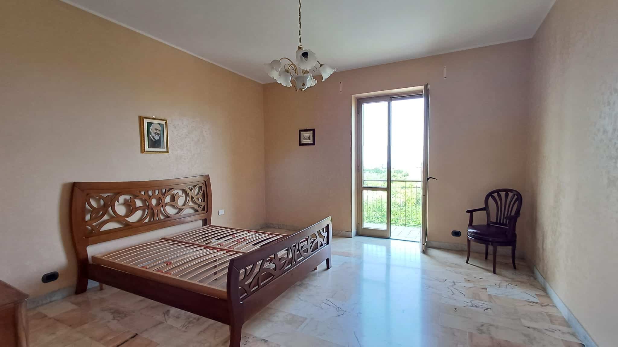 Letto matrimoniale in una stanza luminosa con pareti beige, grande finestra con vista panoramica, arredamento semplice e funzionale, ideale per soggiorno confortevole e rilassante.