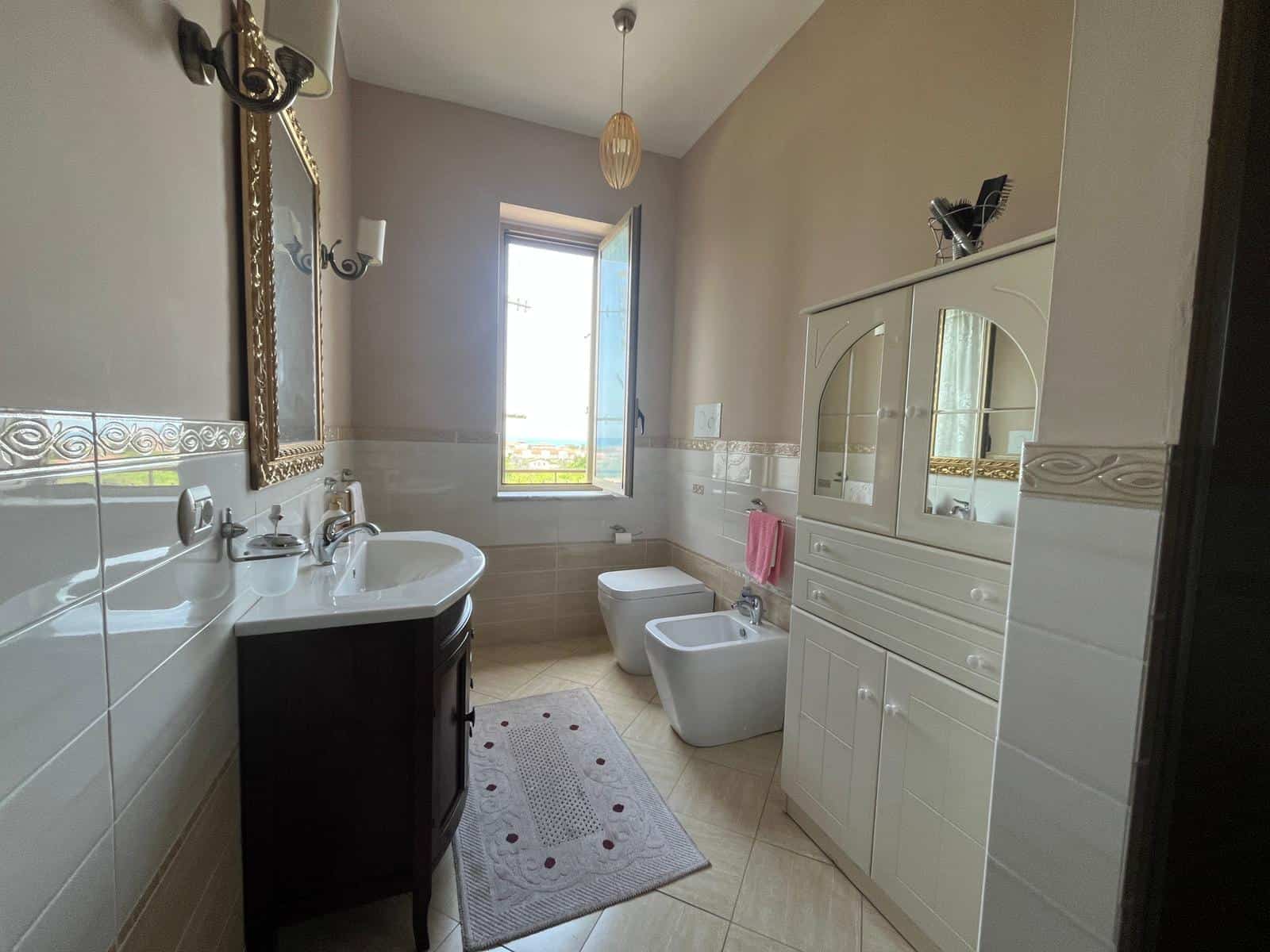 Lavabo e servizi igienici moderni in bagno spazioso con finestra, arredi eleganti e dettagli decorativi, ideale per comfort e funzionalità.