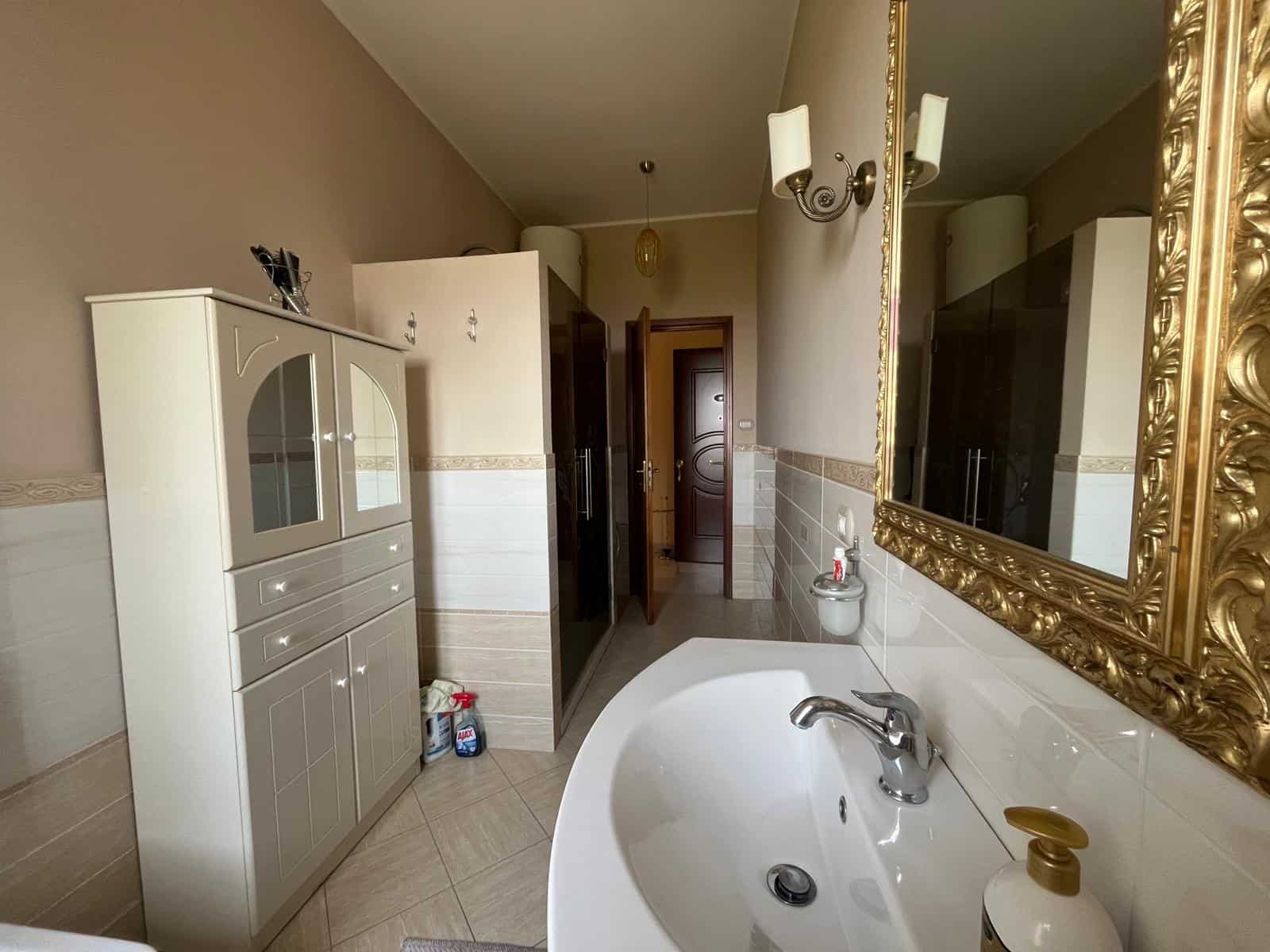 Lavabo moderno con grande specchio dorato, mobili eleganti e dettagli di design in un bagno spazioso e luminoso, ideale per ambienti di alta qualità e comfort.