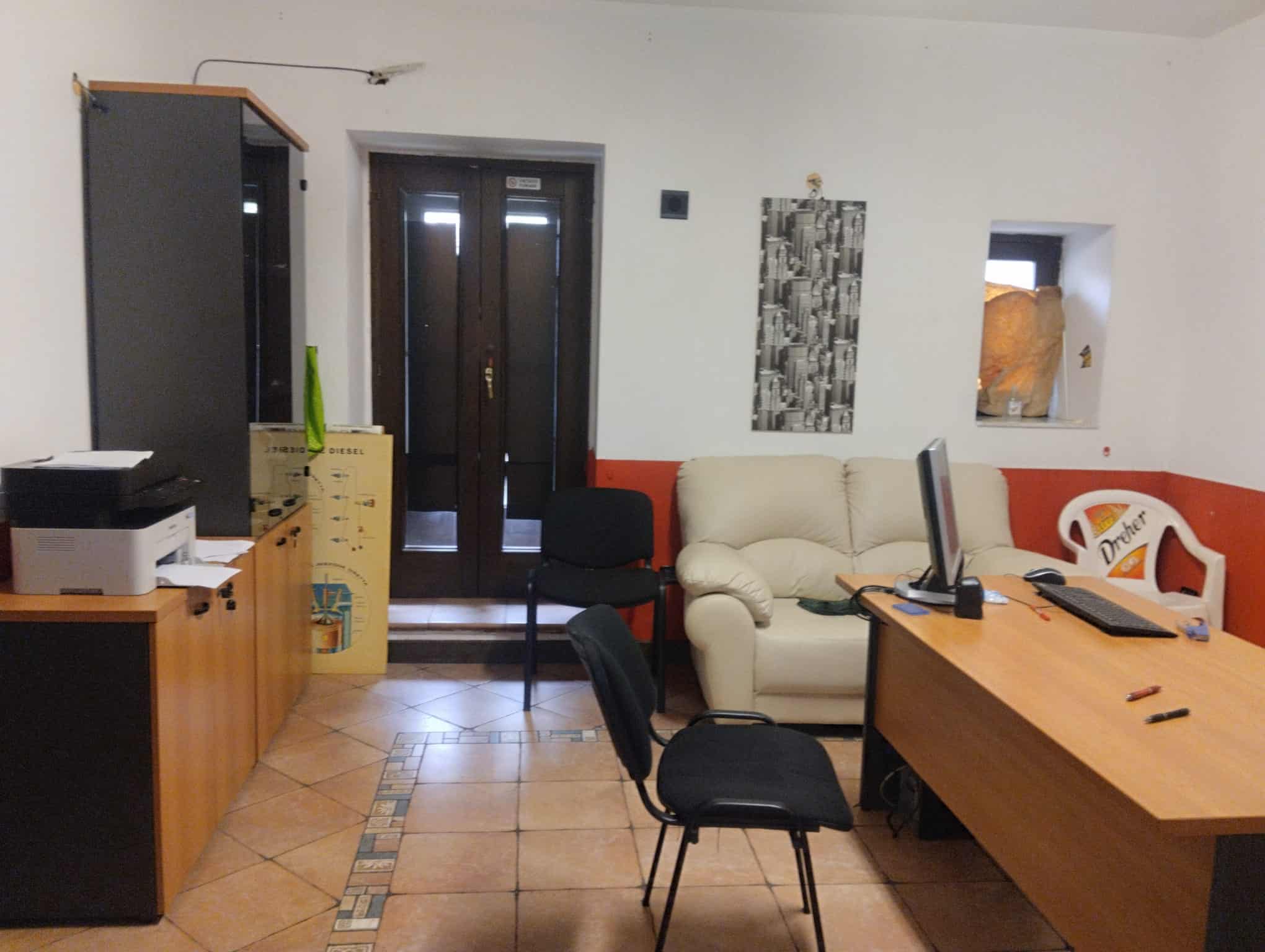 Soggiorno accogliente con divano beige, scrivania e sedie nere, ambiente di lavoro e relax in casa, dettagli di arredo moderni, spazio funzionale e ben illuminato.