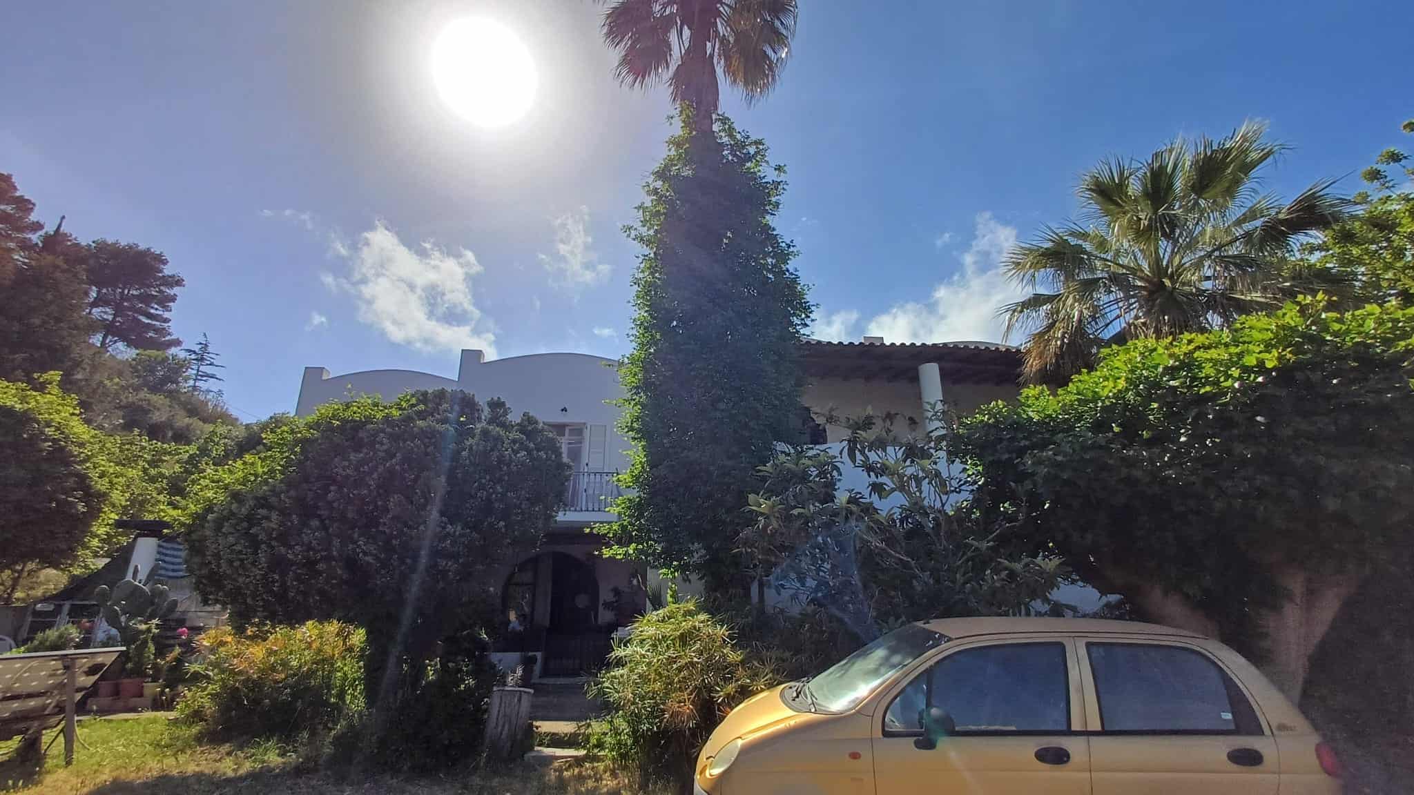Elegante casa moderna circondata da giardini verdi e palme, con un cielo sereno e sole splendente, ideale per vivere in tranquillità e comfort.