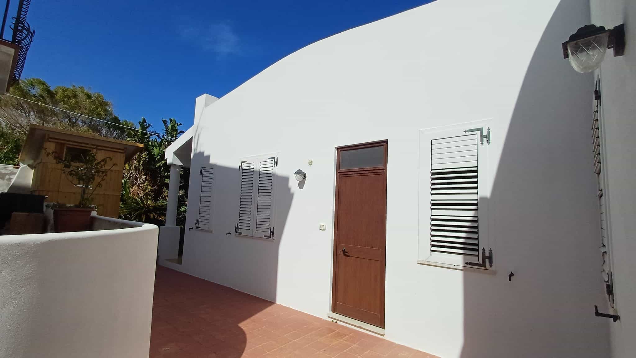 Ampia facciata di casa bianca con porta in legno e finestre con persiane, sotto un cielo azzurro, in stile mediterraneo, ideale per immobili residenziali in Italia.