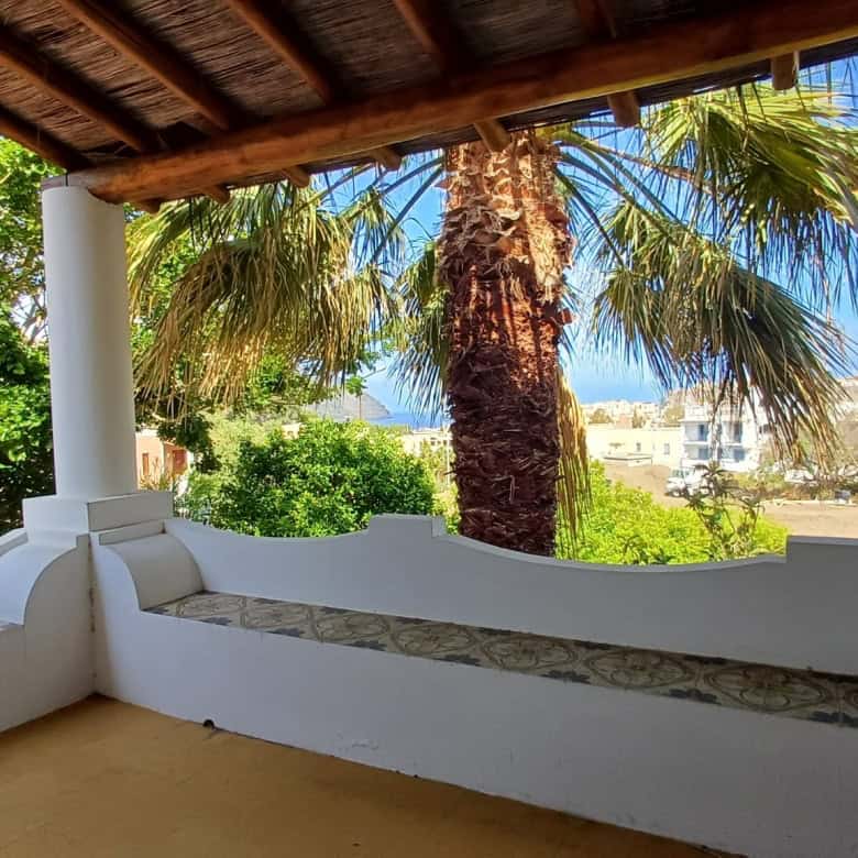 Ampio terrazzo con vista su palme e paesaggio urbano, ideale per relax e convivialità, con copertura in legno e pareti bianche, immerso nel verde e nella natura.