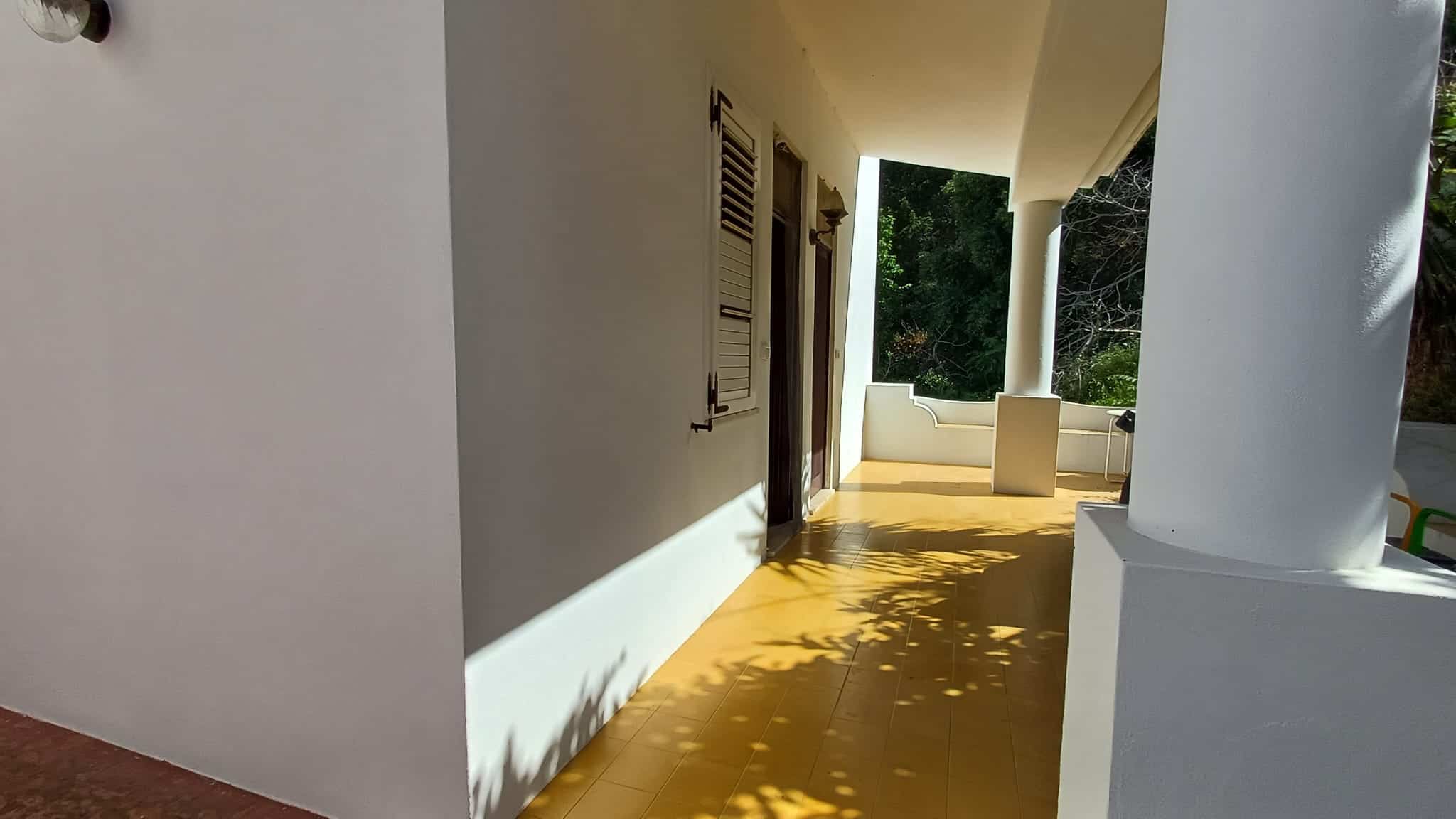 Elegante terrazza esterna con vista verde, pavimentazione in gres color ocra, pareti bianche e colonne classiche, ideale per relax e convivialità all'aperto.