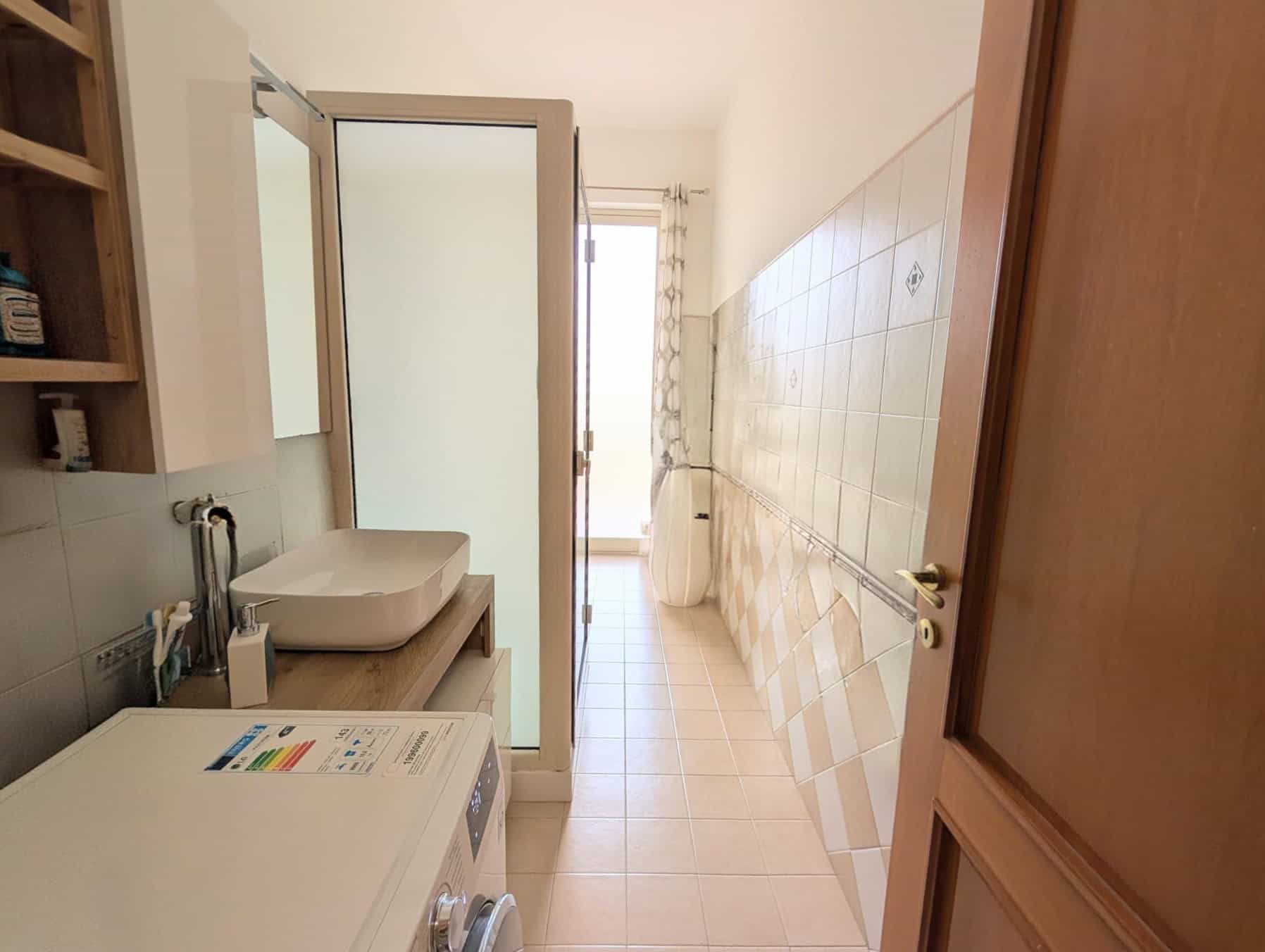 Lavanderia spaziosa con lavatrice, lavabo e armadietti in legno, illuminata da luce naturale, ideale per il lavaggio e la cura dei vestiti in casa.