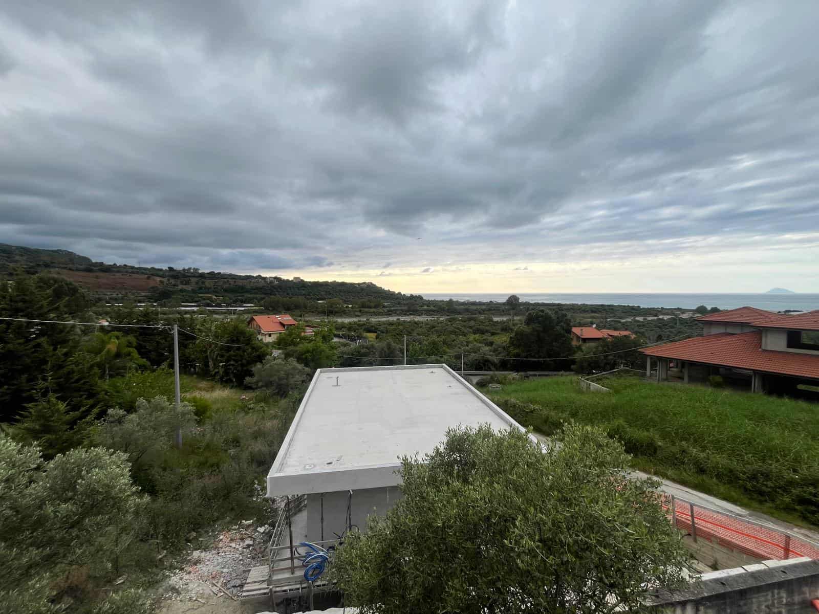 Balcone con vista panoramica sulla campagna e il mare, cielo nuvoloso, in un ambiente rurale con case e vegetazione, immagine di un'area residenziale in Italia.