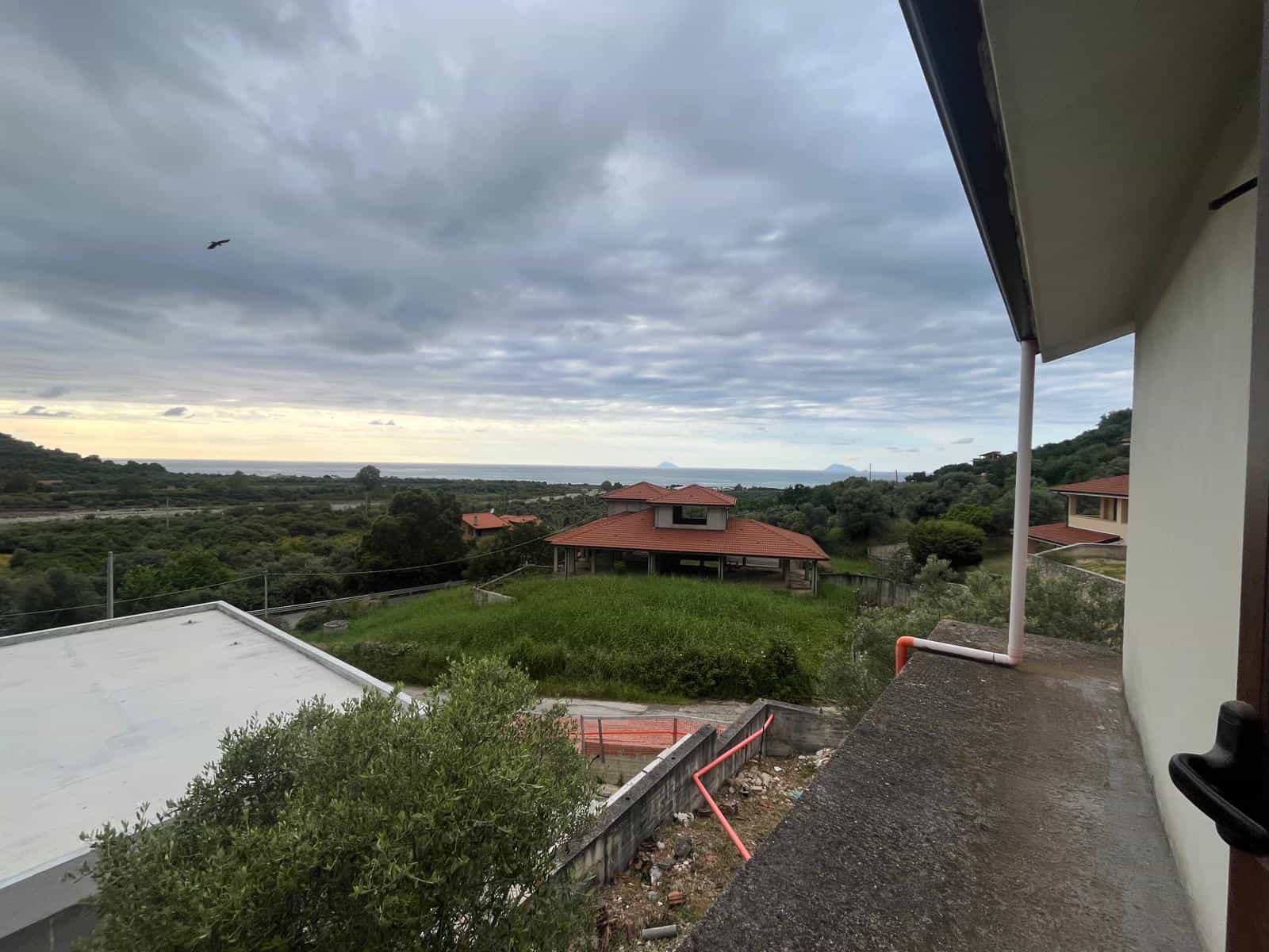 Vista panoramica sulla campagna e il mare da una terrazza di una casa moderna in Italia, con cielo nuvoloso e vegetazione lussureggiante.