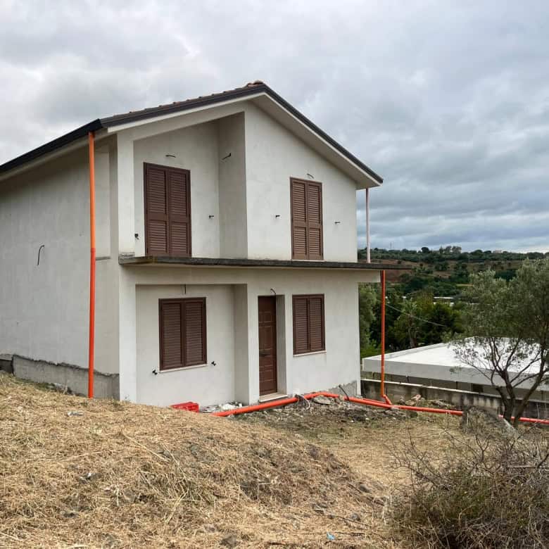 Casa unifamiliare in costruzione su terreno collinare con vista panoramica, pareti bianche e finestre con persiane in legno, ambiente rurale e tranquillo.