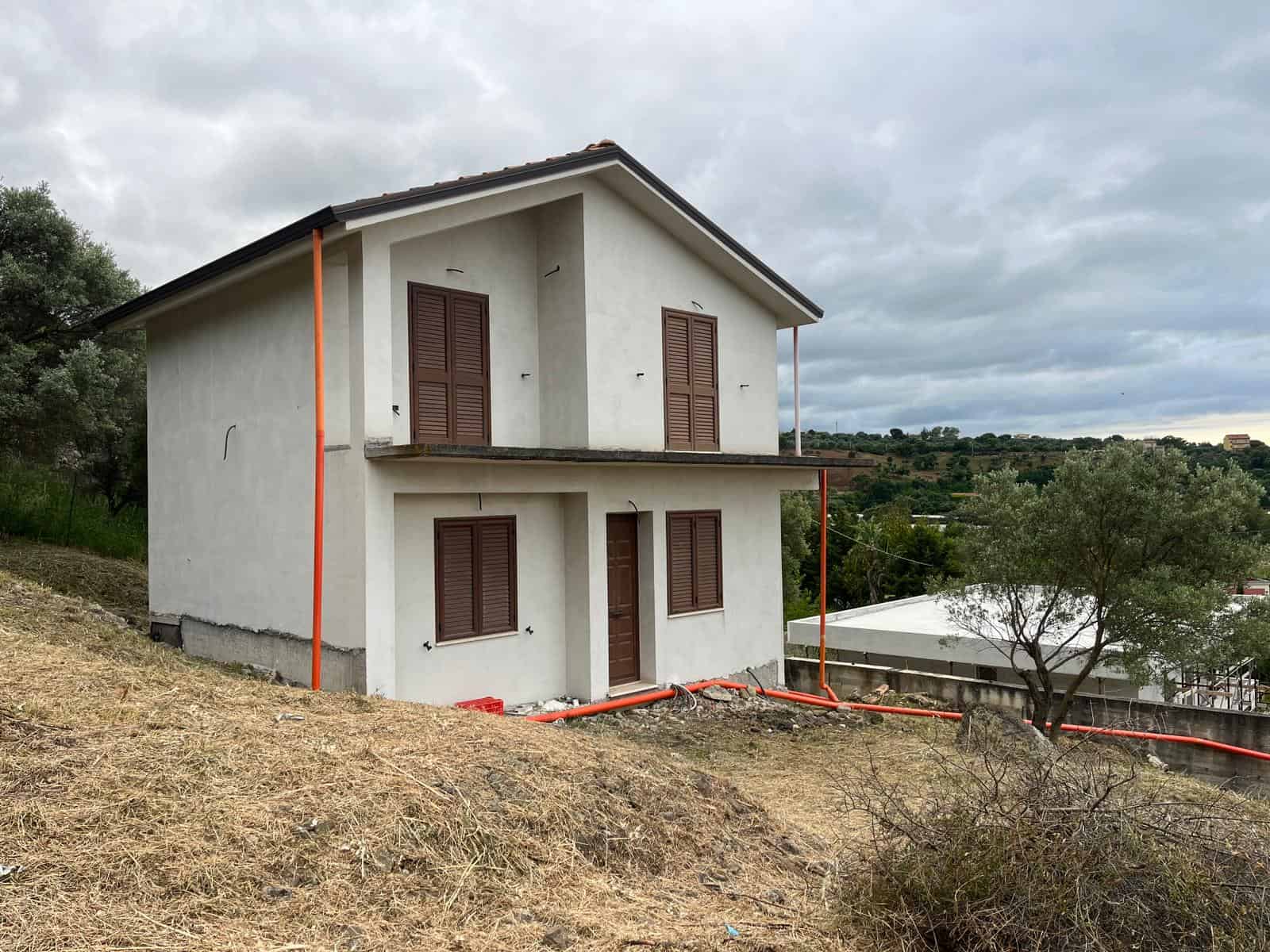 Casa unifamiliare in costruzione su terreno collinare con vista panoramica, pareti bianche e finestre con persiane in legno, ambiente rurale e tranquillo.