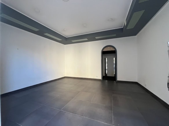 Ampia stanza vuota con pareti bianche, soffitto decorato e pavimento in piastrelle scure, ideale per arredamento moderno e personalizzato.
