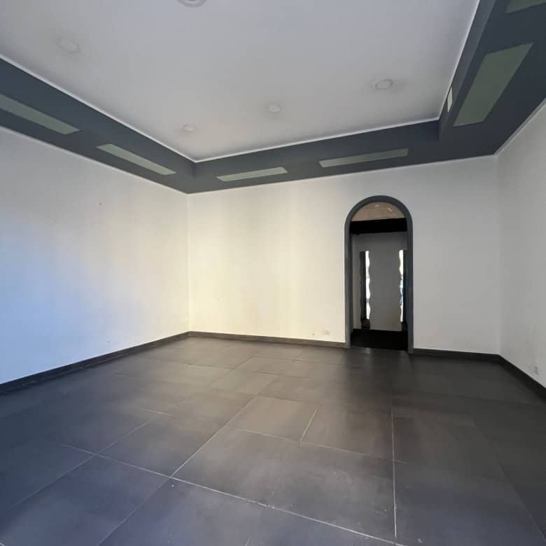 Ampia stanza vuota con pareti bianche, soffitto decorato e pavimento in piastrelle scure, ideale per arredamento moderno e personalizzato.