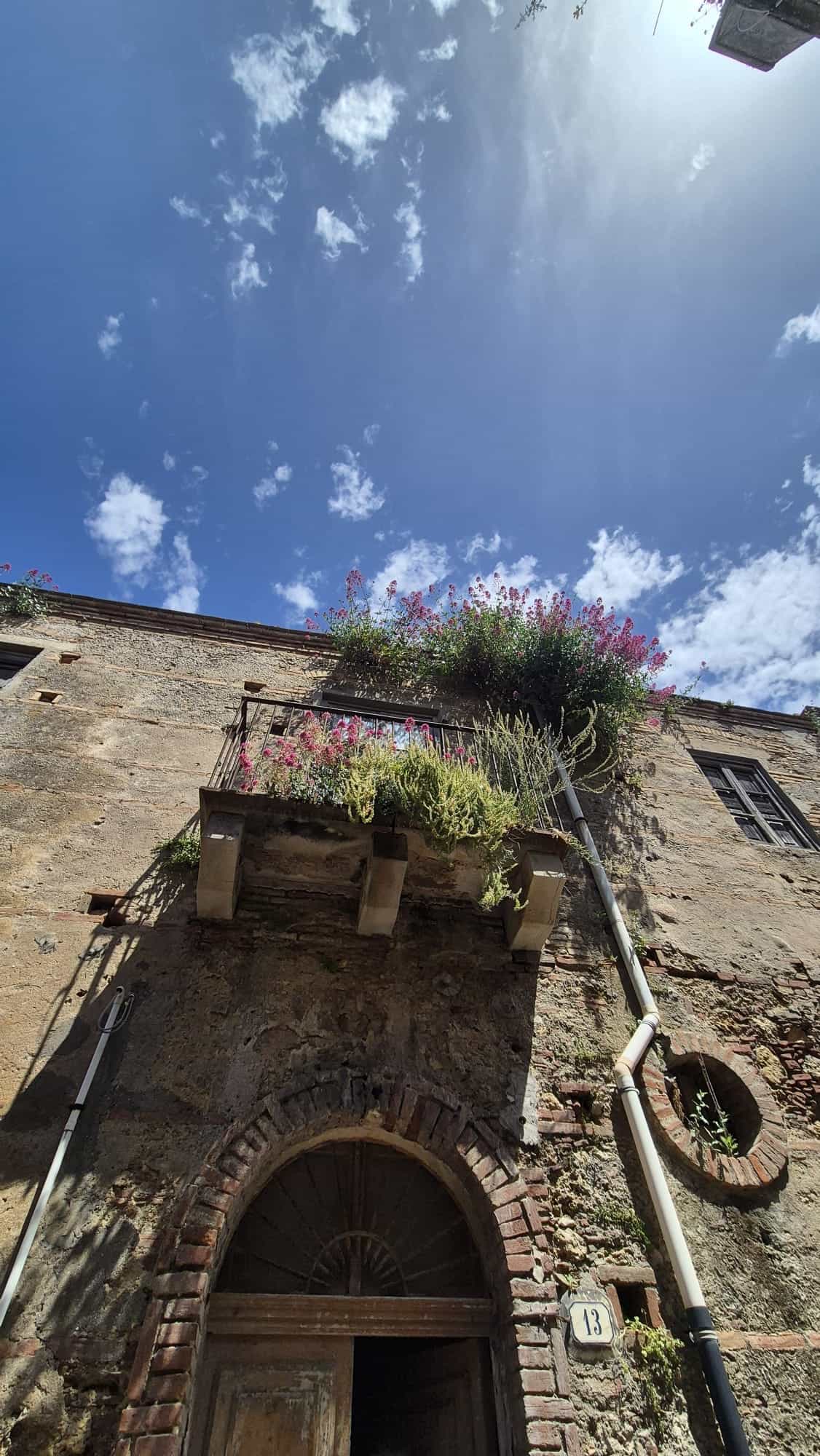 Il cielo azzurro con nuvole bianche sopra un edificio storico con balcone fiorito, in un'immagine che evidenzia l'architettura tradizionale italiana e il fascino delle case antiche.