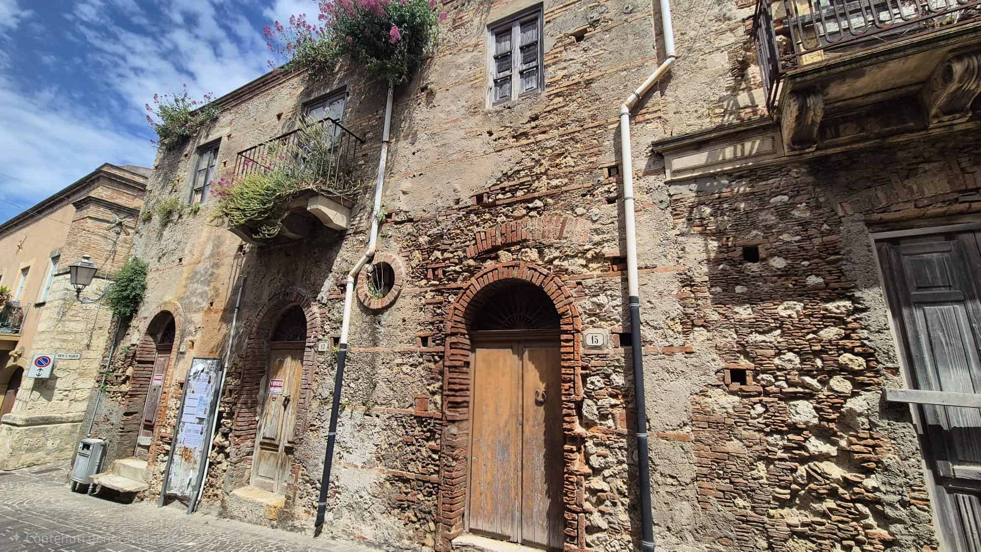 Facciata di un edificio storico in pietra con porte in legno e dettagli architettonici antichi, in un quartiere caratteristico italiano.