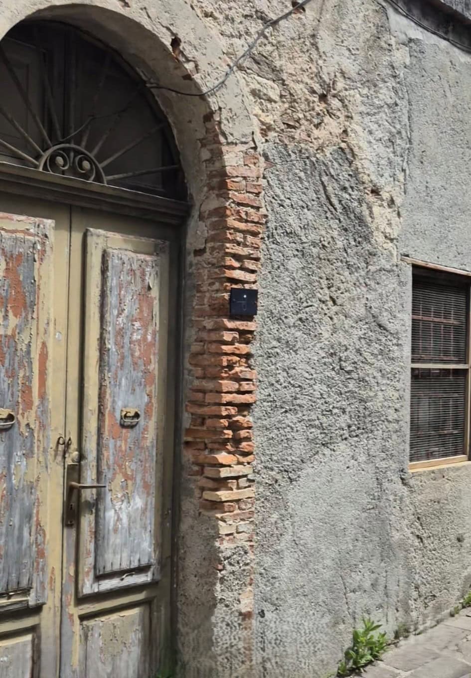 Porta in legno vecchia con dettagli di ferro battuto, affiancata da parete in pietra e mattoni, in un edificio storico italiano.