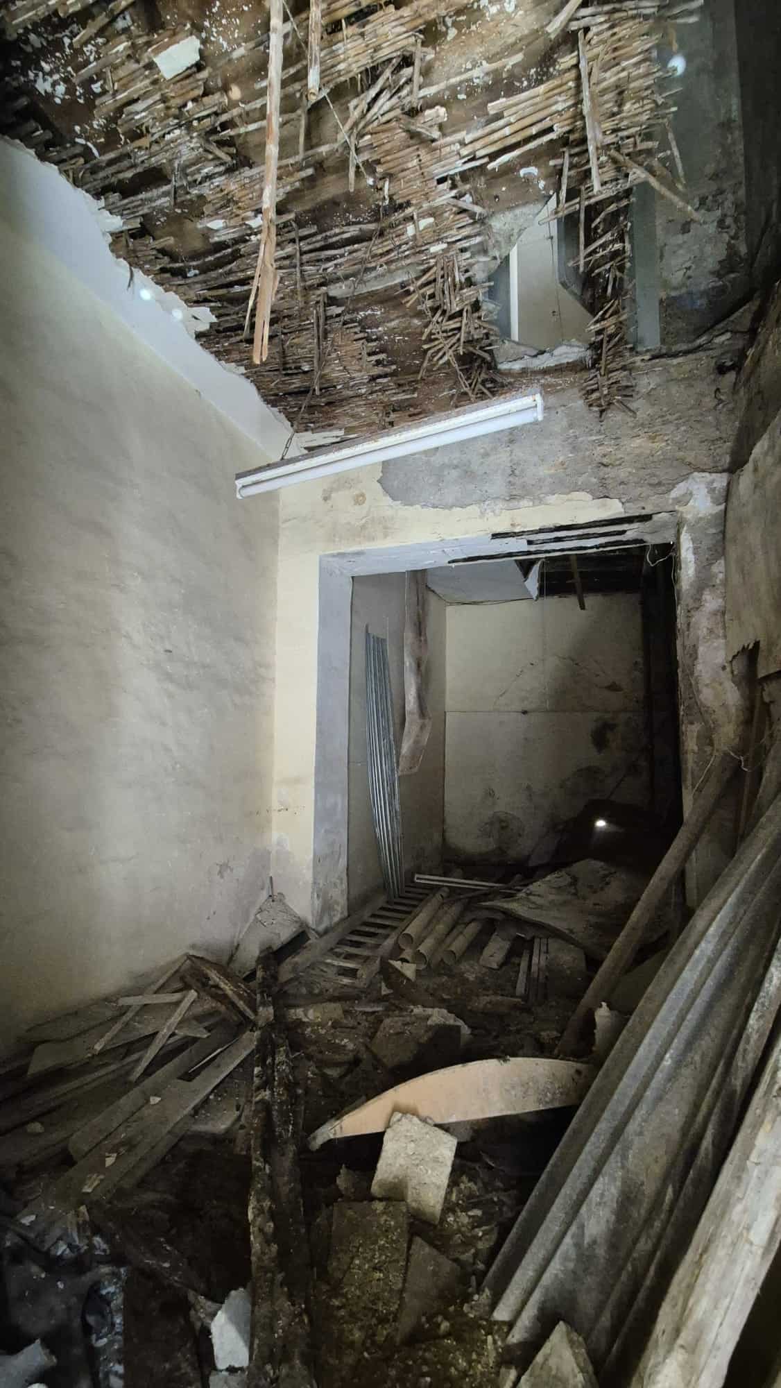 Disastro strutturale in un edificio storico con soffitto crollato, detriti e materiali di costruzione sparsi, evidenziando lavori di ristrutturazione e necessità di interventi di sicurezza e restauro.