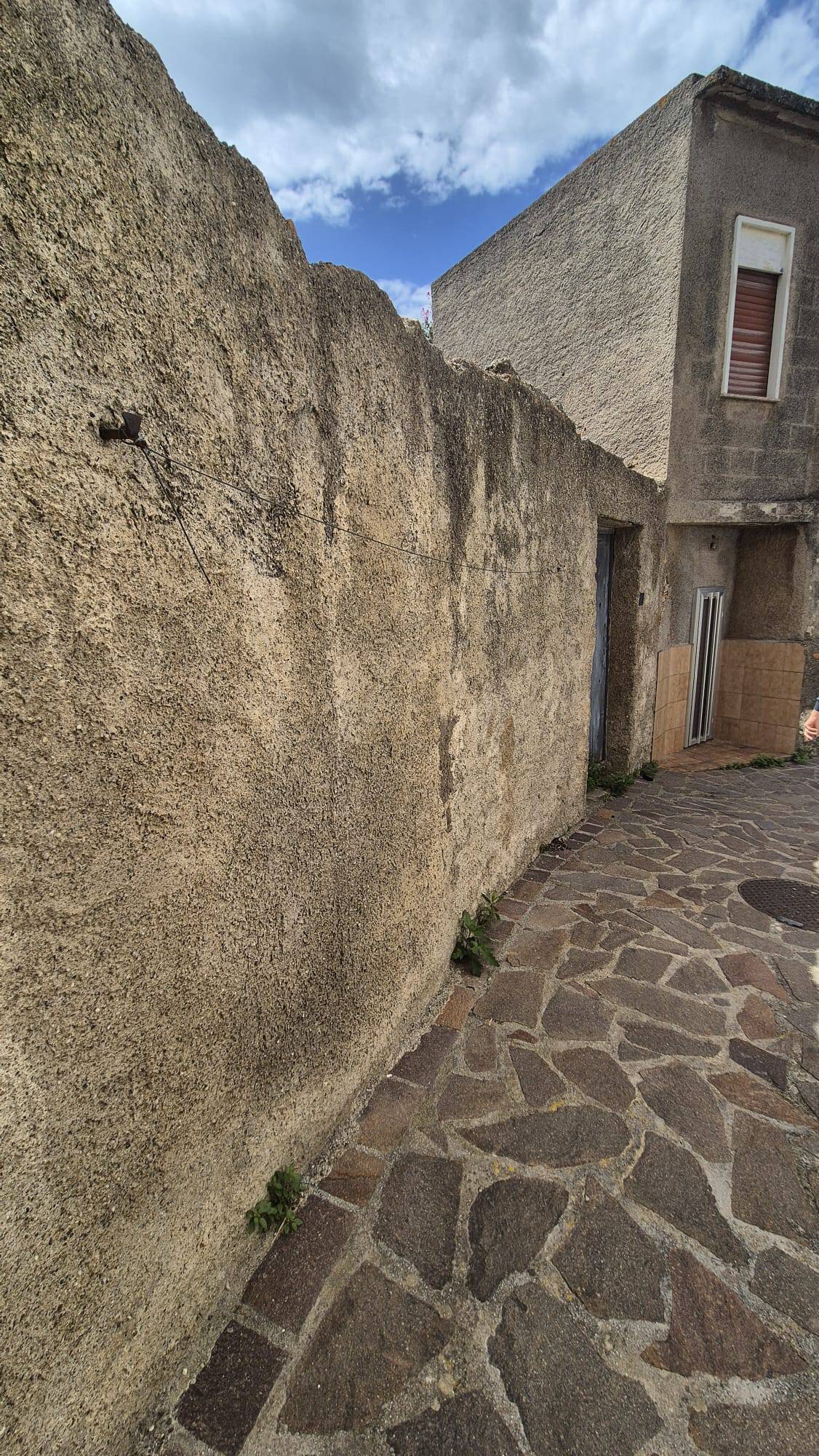 Antico muro in pietra e strada pavimentata in ciottoli, scenario di un vicolo storico in un quartiere italiano.