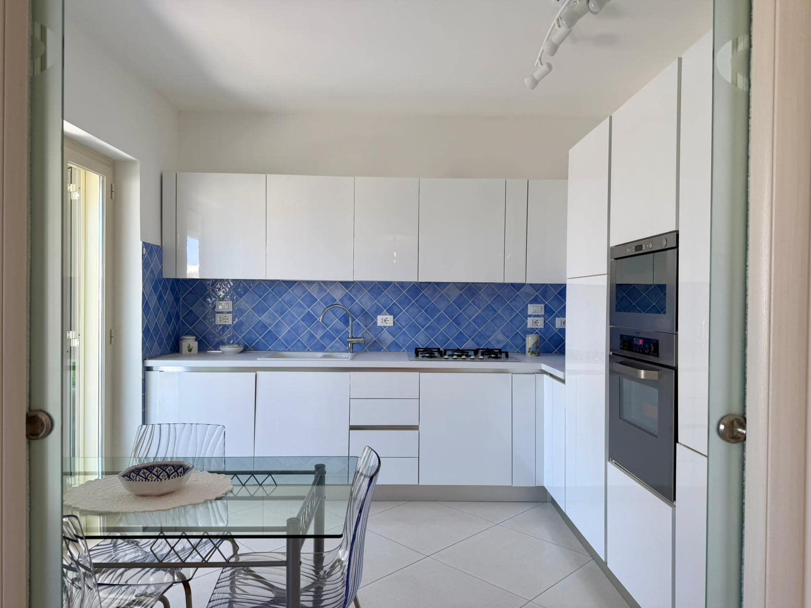 Moderna cucina bianca con piano cottura a gas e forno integrato, arredamento minimalista e spazioso, ideale per case moderne e funzionali, con accesso a balcone luminoso.
