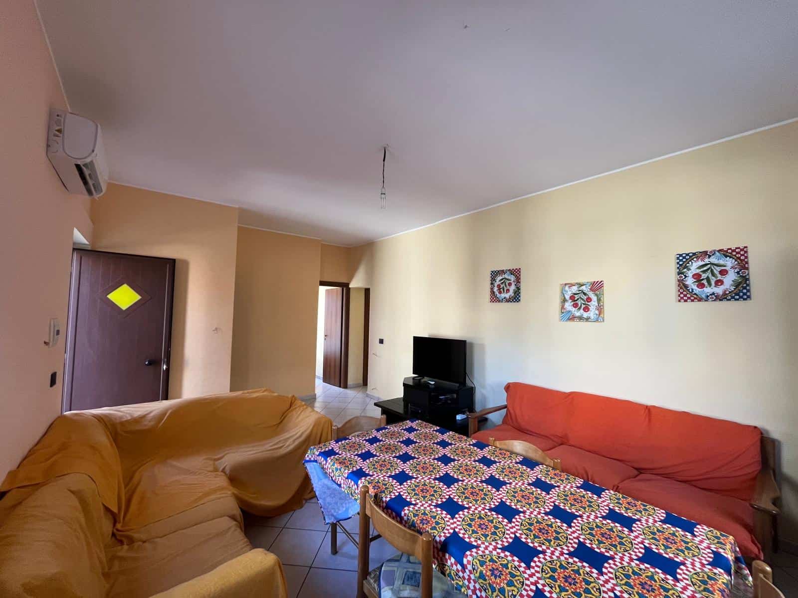 Soggiorno luminoso con divani e tavolo da pranzo decorato, arredamento accogliente, TV e pareti decorate con quadri colorati, ambiente caldo e invitante.