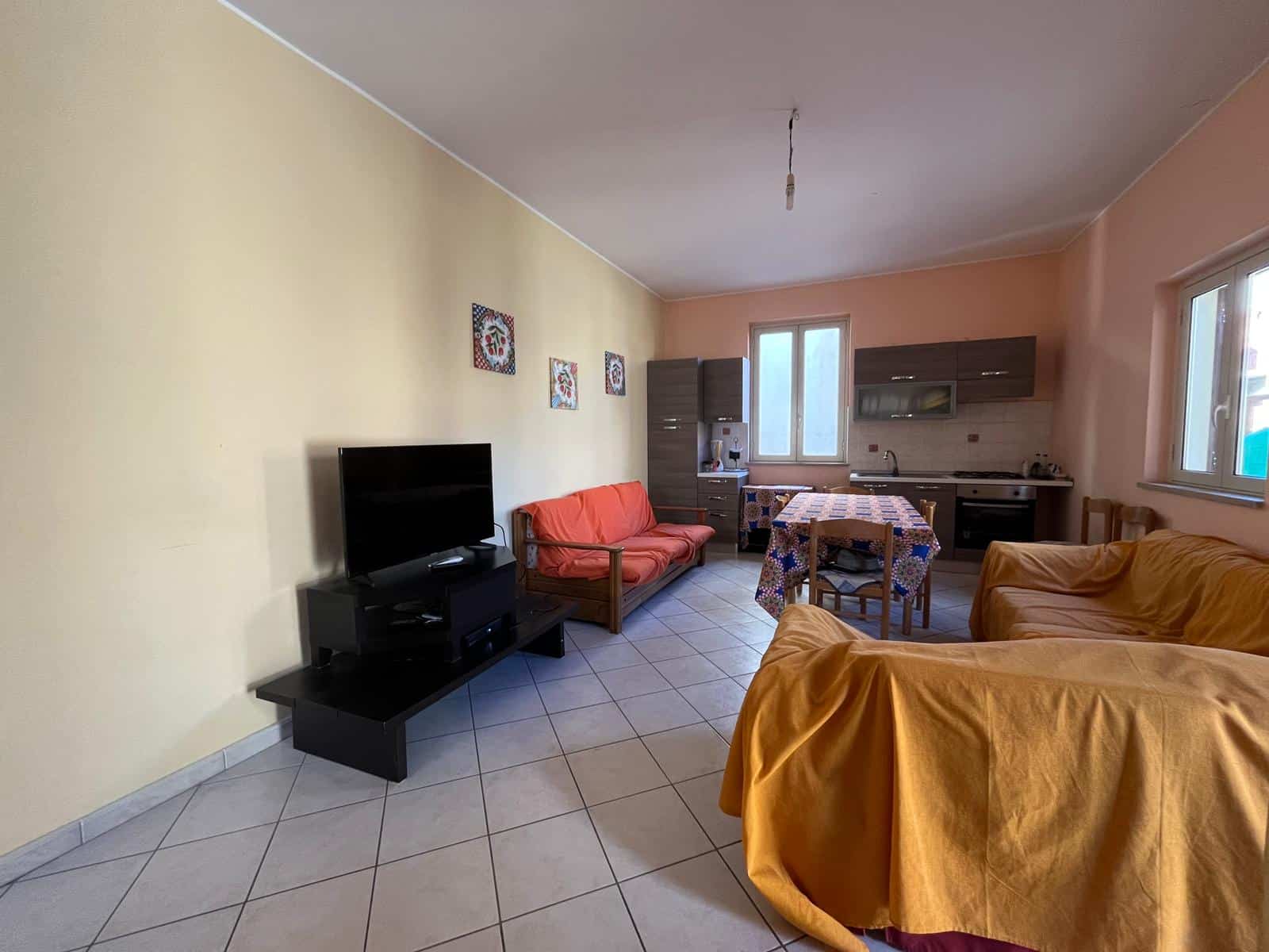 Interno di un soggiorno spazioso con divani, TV e zona cucina, illuminato da grandi finestre, arredamento funzionale e pareti colorate, ideale per vivere in comfort.