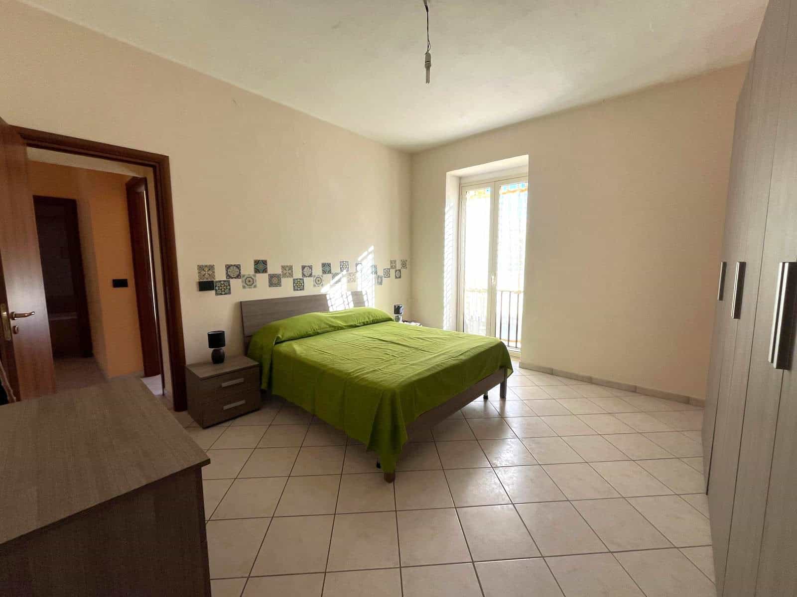 Letto matrimoniale con lenzuola verdi in camera spaziosa e luminosa, con armadio e accesso a balcone, ideale per affitti turistici o residenziali, rappresenta un'opportunità di investimento immobiliar.