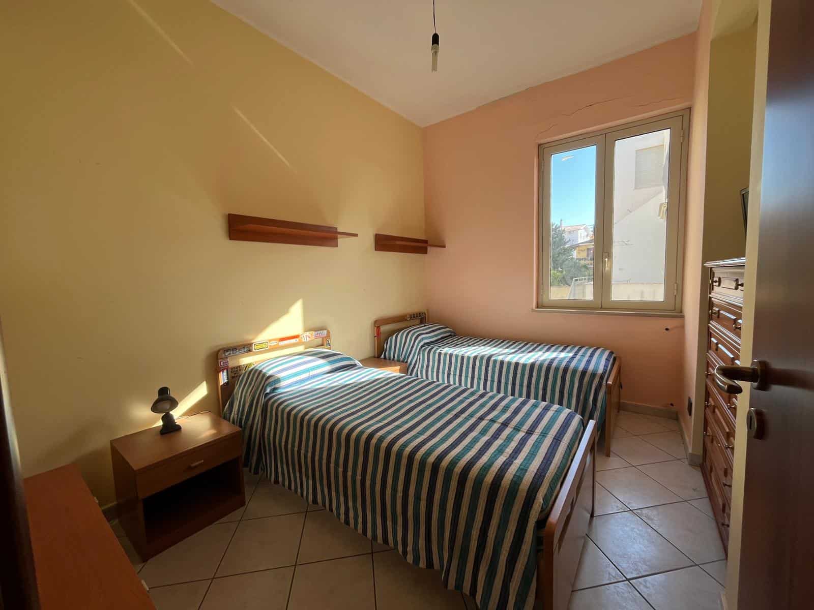 Camera da letto con due letti singoli, pareti colorate e finestra che lascia entrare luce naturale, arredamento semplice e funzionale.