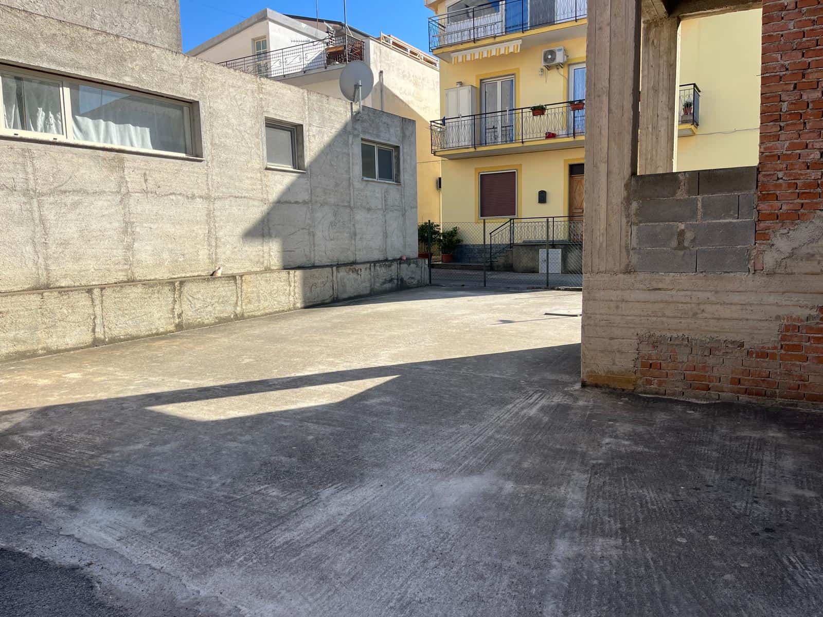 Ampio cortile esterno in zona urbana con edifici residenziali, pavimentato in cemento, ideale per parcheggio o spazio ricreativo, con luce naturale e ambiente tranquillo.