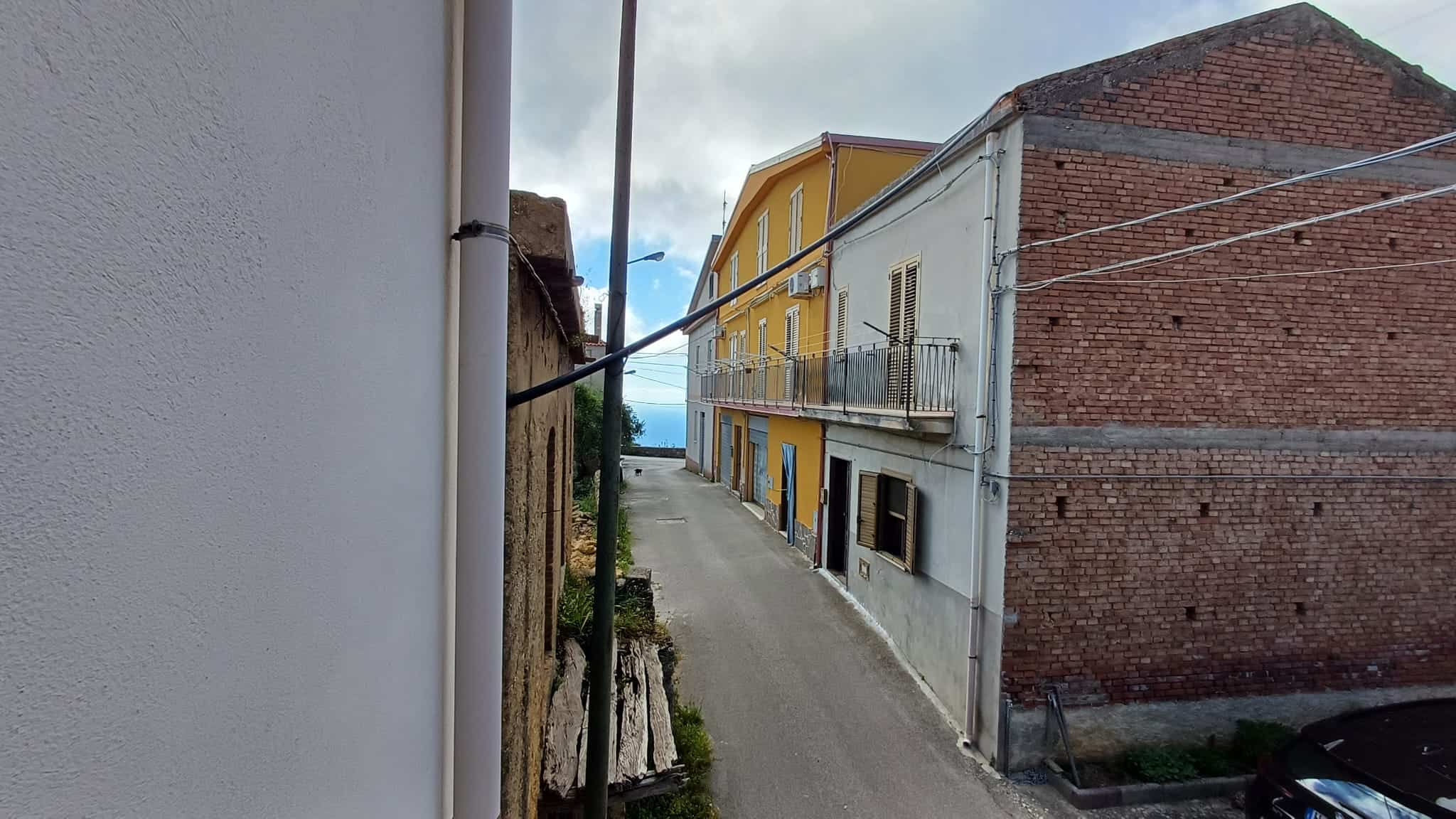 Ampia strada urbana tra edifici residenziali in stile italiano, con cielo nuvoloso e vista verso l'orizzonte, in un quartiere tranquillo e pittoresco.