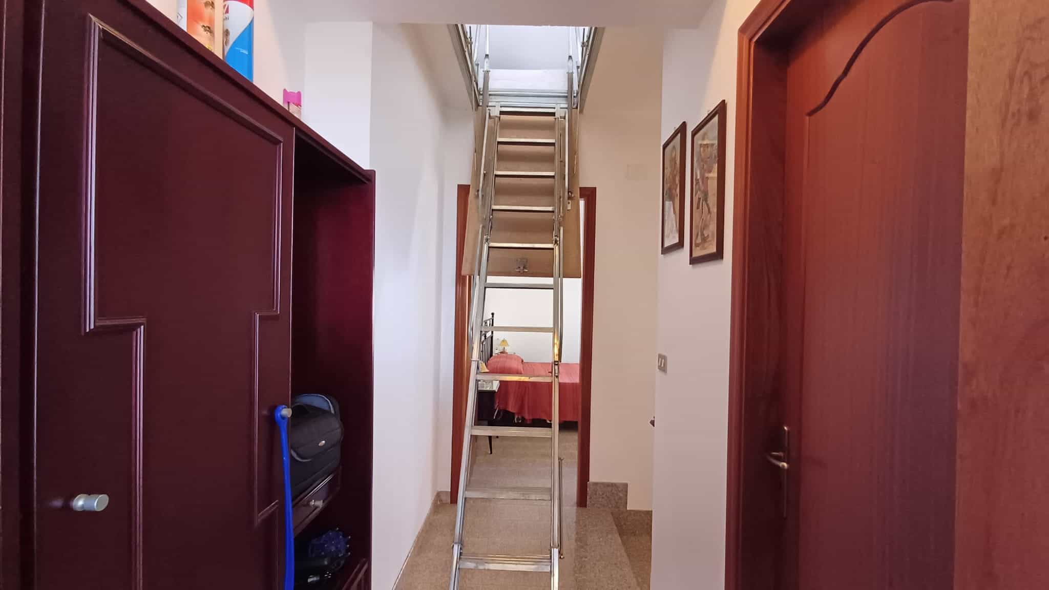 Spazio interno di un appartamento con scala retrattile, pareti decorate con quadri, porta in legno e armadio a muro, ambiente luminoso e accogliente, ideale per soluzioni di arredamento moderne e funz.