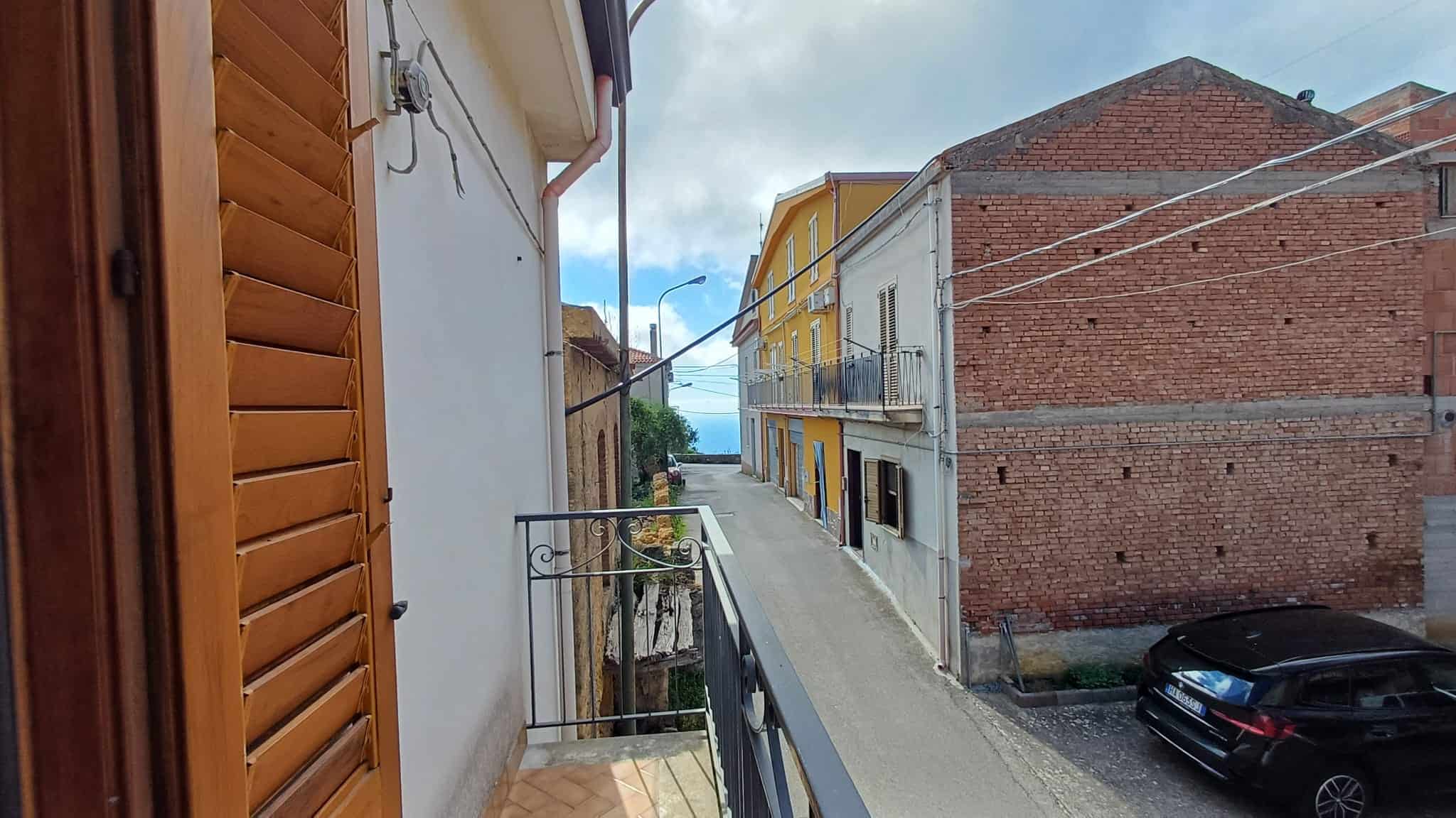 Ampia veduta di un vicolo urbano con edifici colorati e auto parcheggiate, vista verso il mare in lontananza, in un quartiere residenziale di città costiera italiana.