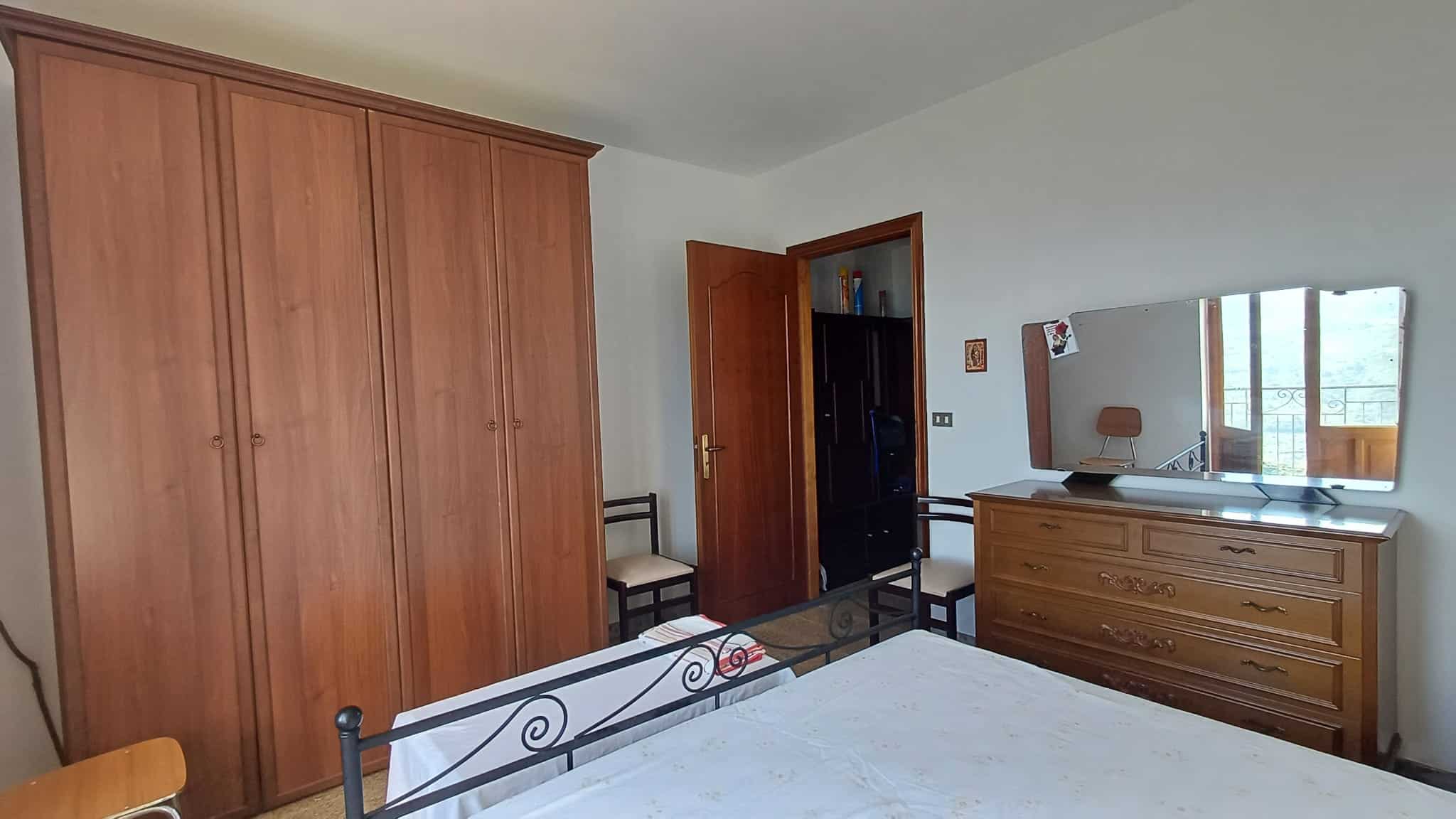 Ampia camera da letto con armadio in legno, letto in ferro battuto e finestra che permette l'ingresso di luce naturale, ideale per ambienti residenziali e affitti turistici.