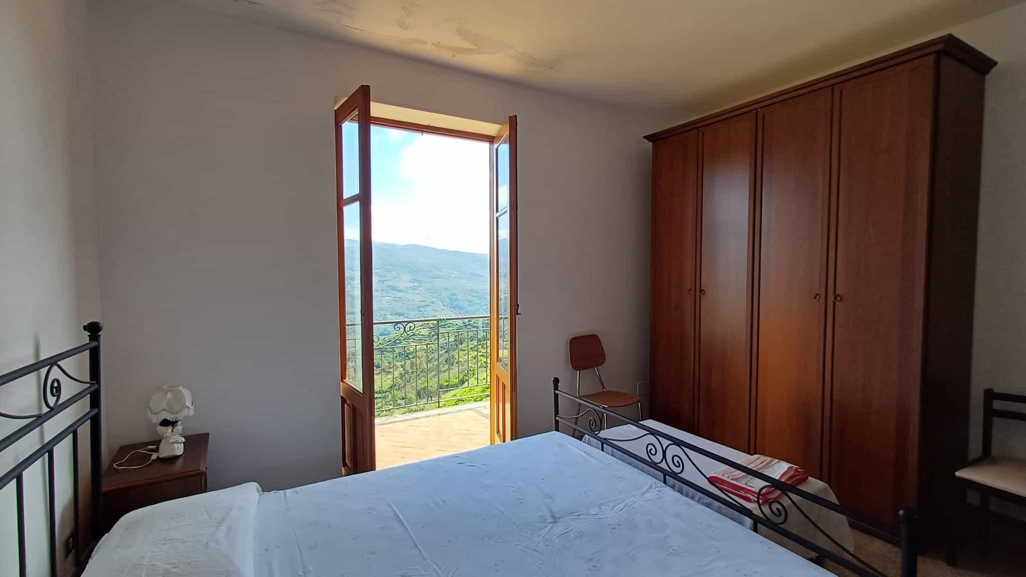 Ampia camera da letto con finestra aperta che offre una vista panoramica sulle colline e il cielo azzurro, arredi eleganti e atmosfera accogliente.