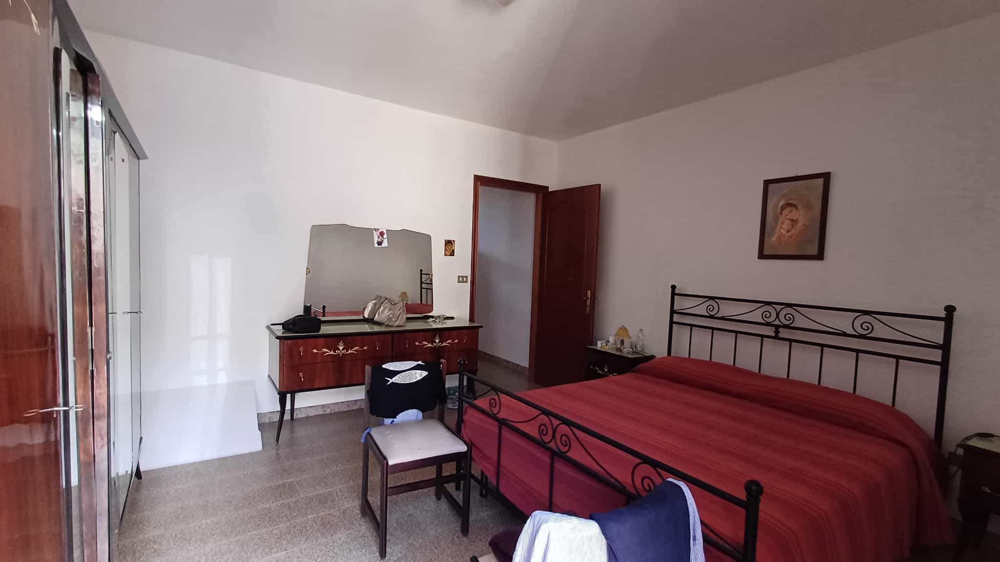 Ampia camera da letto con letto matrimoniale, armadio a specchio e mobiletto con specchio, decorata con quadro alle pareti, in stile semplice e funzionale.