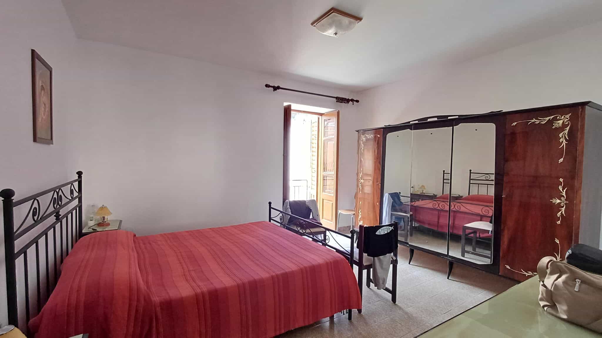 Ampia camera da letto con letto matrimoniale, armadio antico e finestra che permette l'ingresso di luce naturale, ideale per affitti di case vacanza o residenziali di charme.