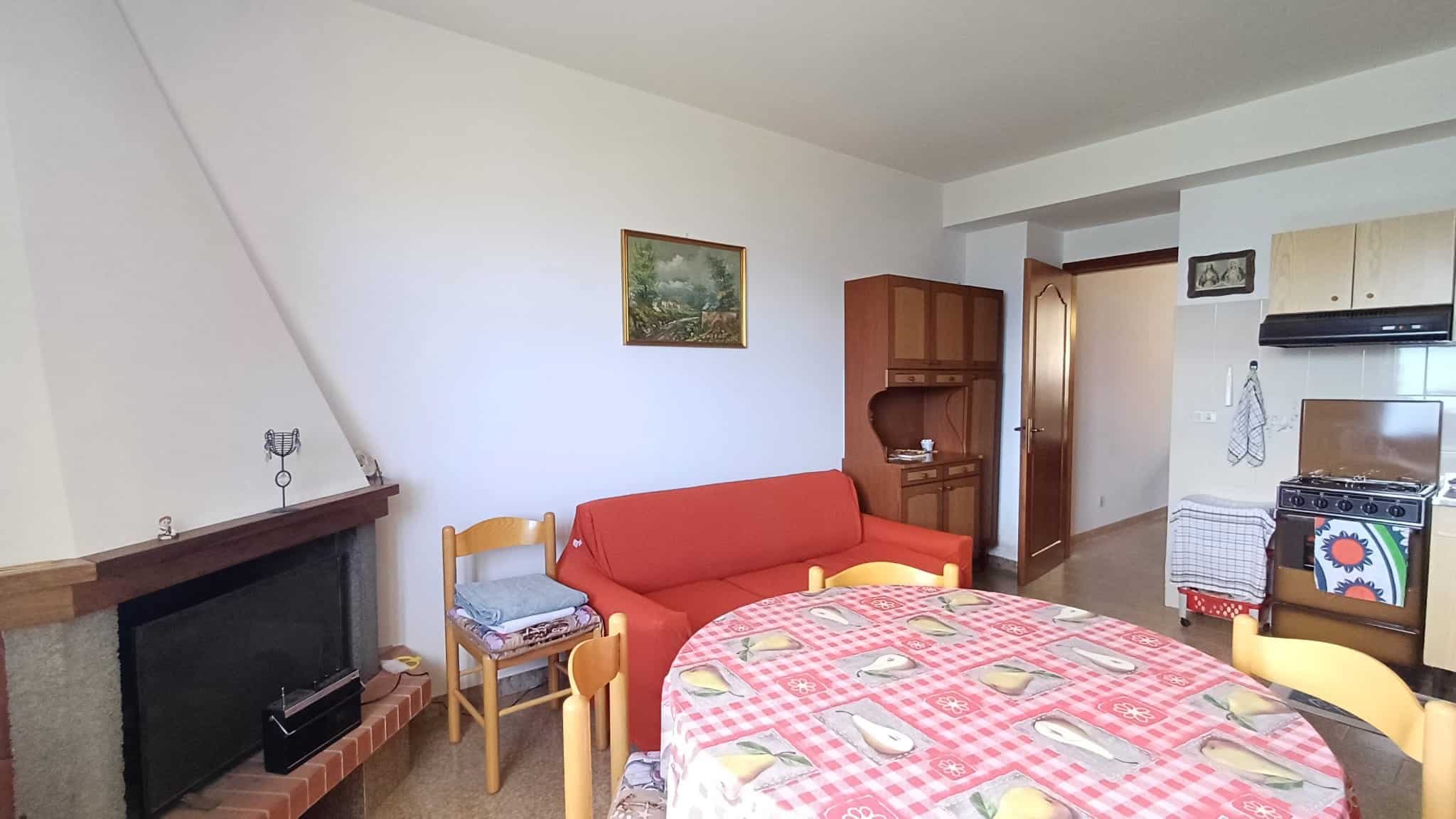 Soggiorno con divano rosso, tavolo da pranzo con tovaglia a quadri, cucina moderna e arredi accoglienti in un appartamento NextCasa, soluzione ideale per affitti a breve termine.
