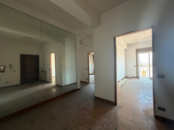 Interno di un appartamento in fase di ristrutturazione con pareti bianche, grandi finestre e pavimento in piastrelle, pronto per essere arredato.