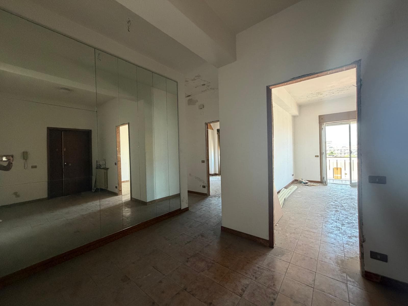 Interno di un appartamento in fase di ristrutturazione con pareti bianche, grandi finestre e pavimento in piastrelle, pronto per essere arredato.